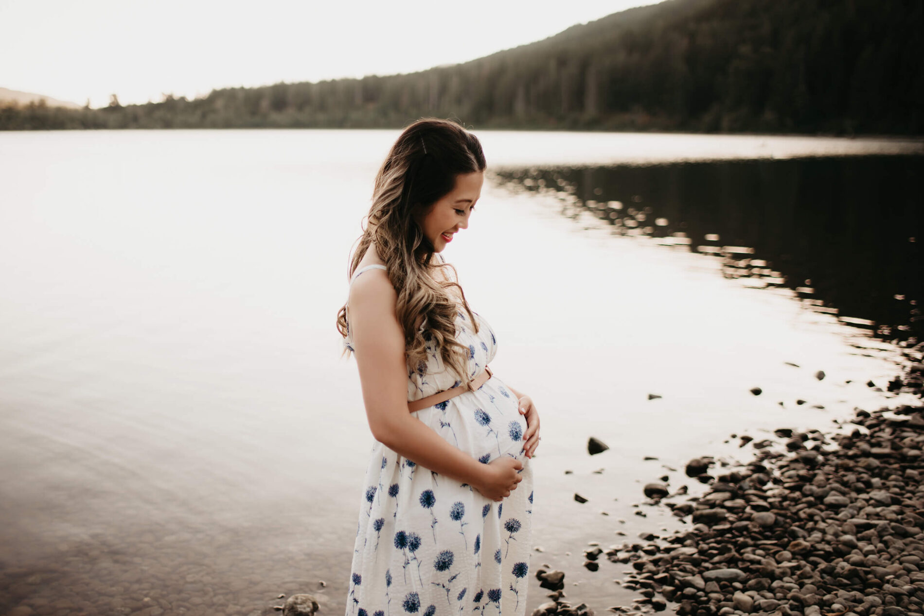 Best places for maternity photo shoot in Seattle, pregnant woman in a cute standing on the beach of a lake with Cascades in the background