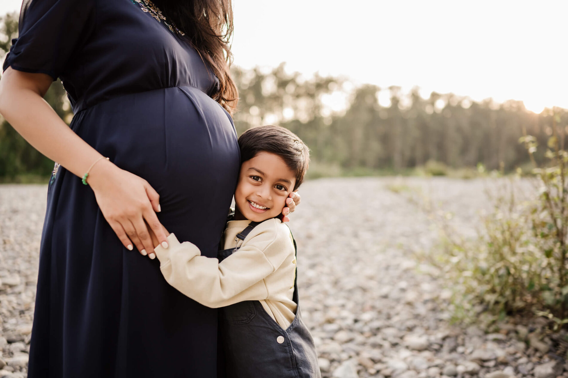 Moment during a maternity photo shoot of a happy toddler hugging mom's belly