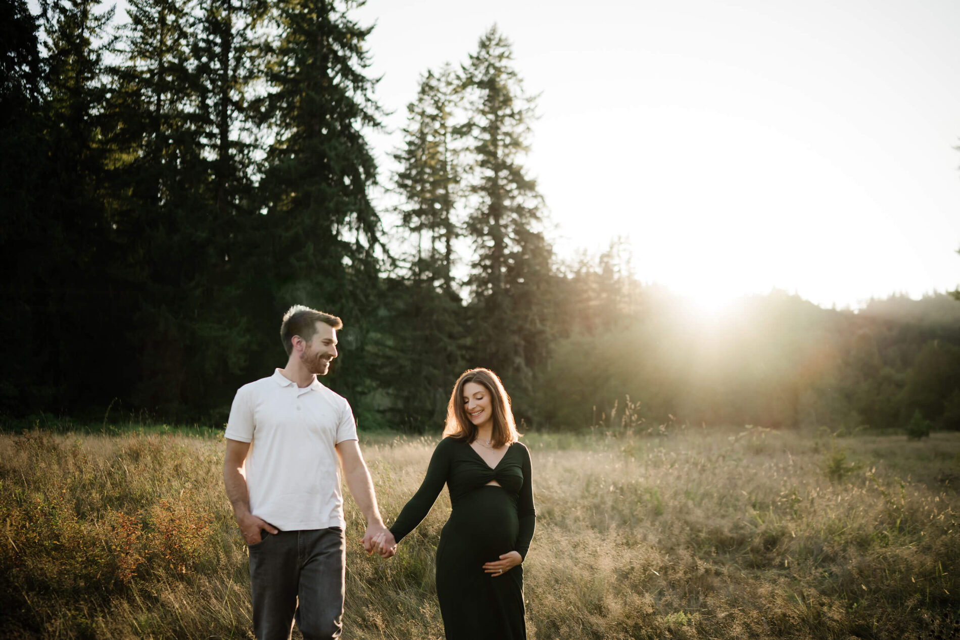 Maternity photo shoot posing idea, couple holding hands, walking through a field of tall grass during sunset