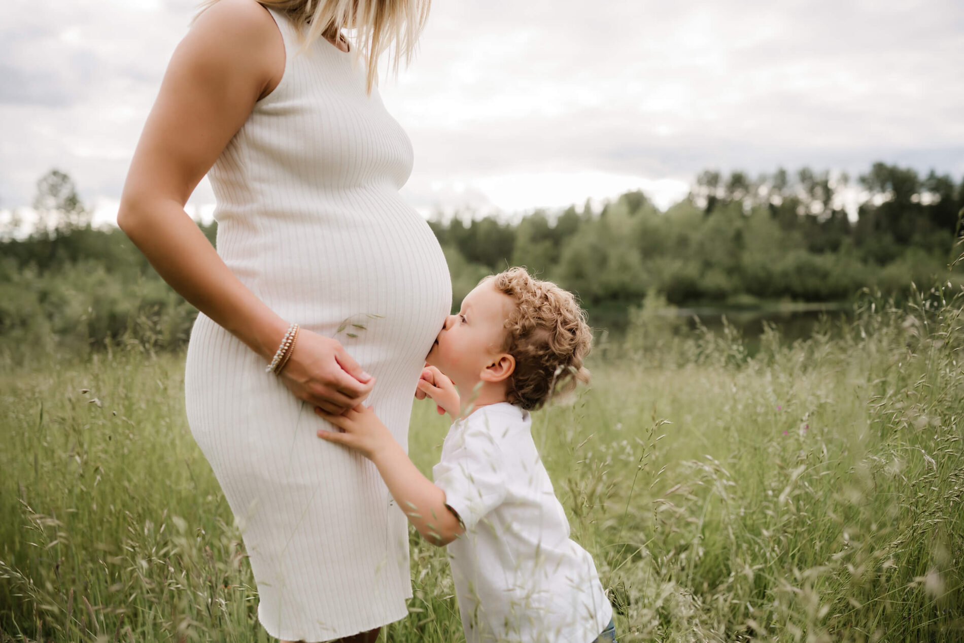 Maternity photo posing idea for mom and toddler, a boy kissing mom's belly in a field