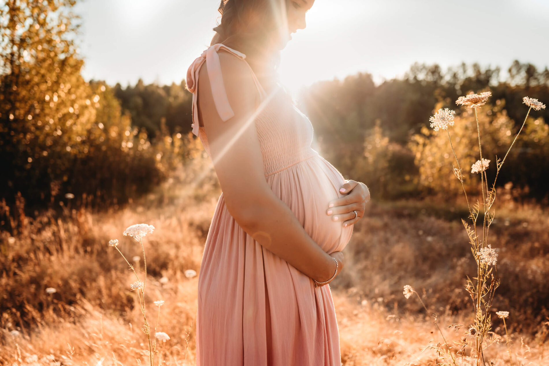 Pregnant woman in a pink dress posing in a field of wildflowers in Redmond during golden hour