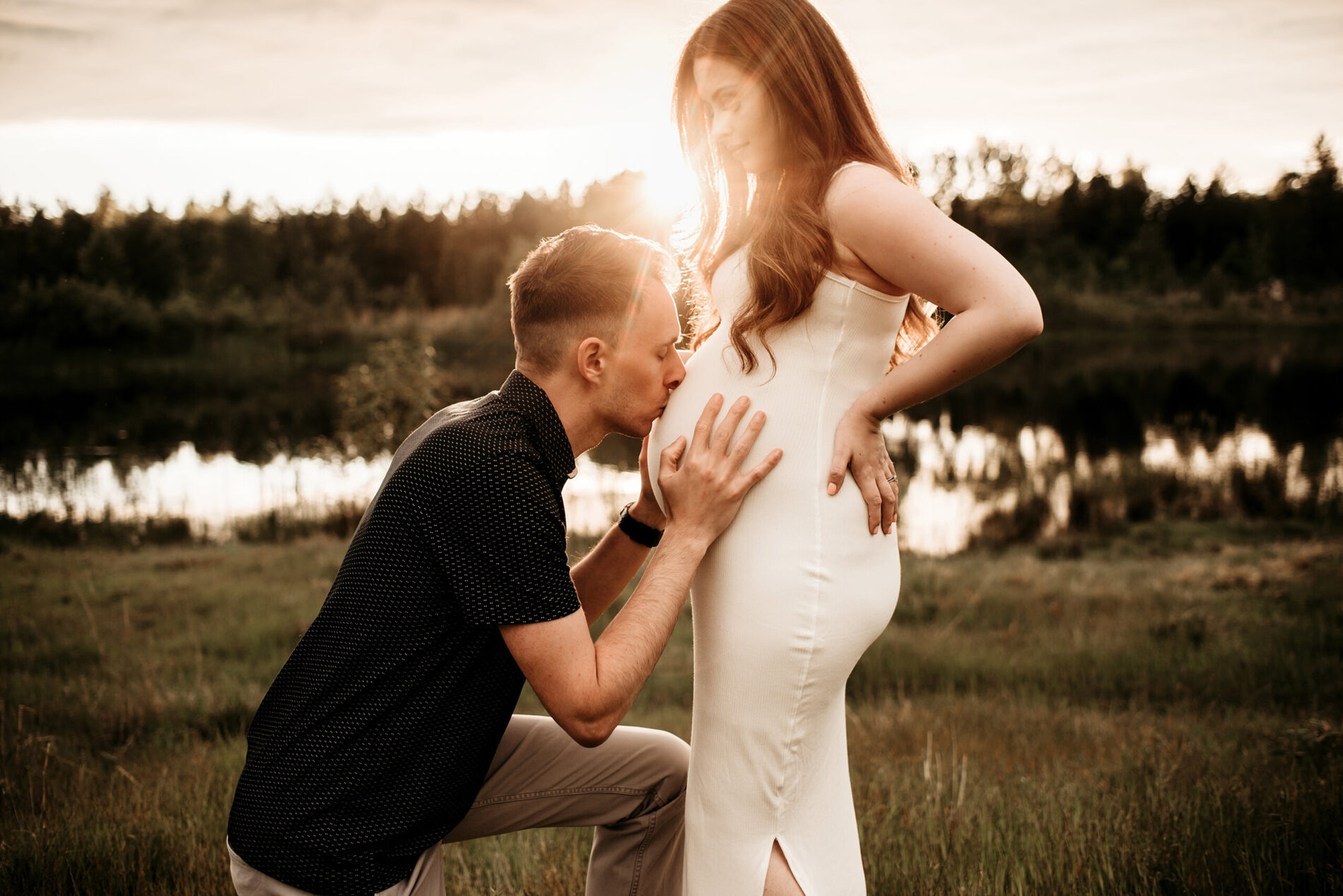Maternity photo shoot posing idea, husband kneeling kissing wife's belly, beautiful field during sunset