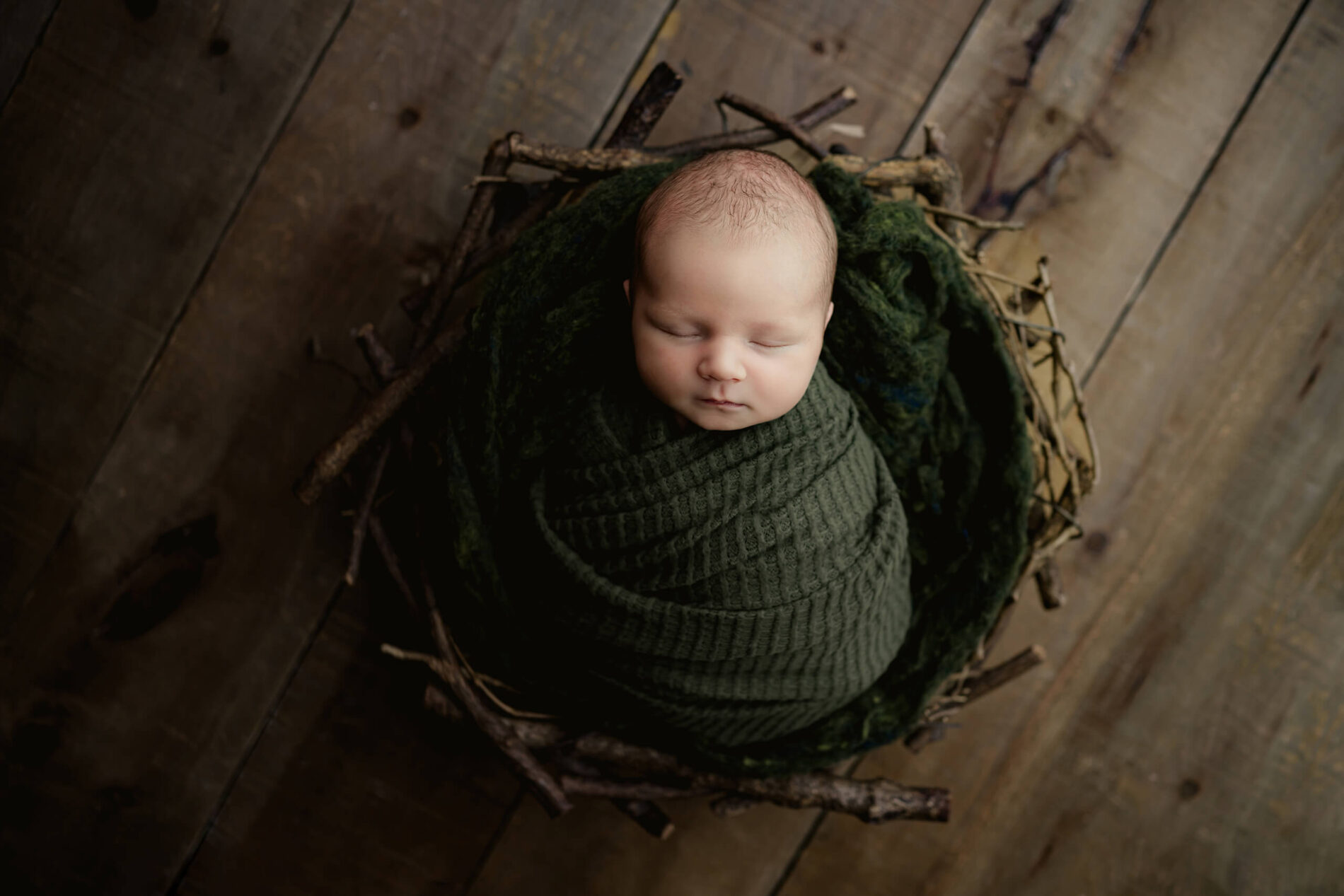 Unique newborn photography with props, baby boy wrapped in green blanket and posed in a basket that looks like a nest