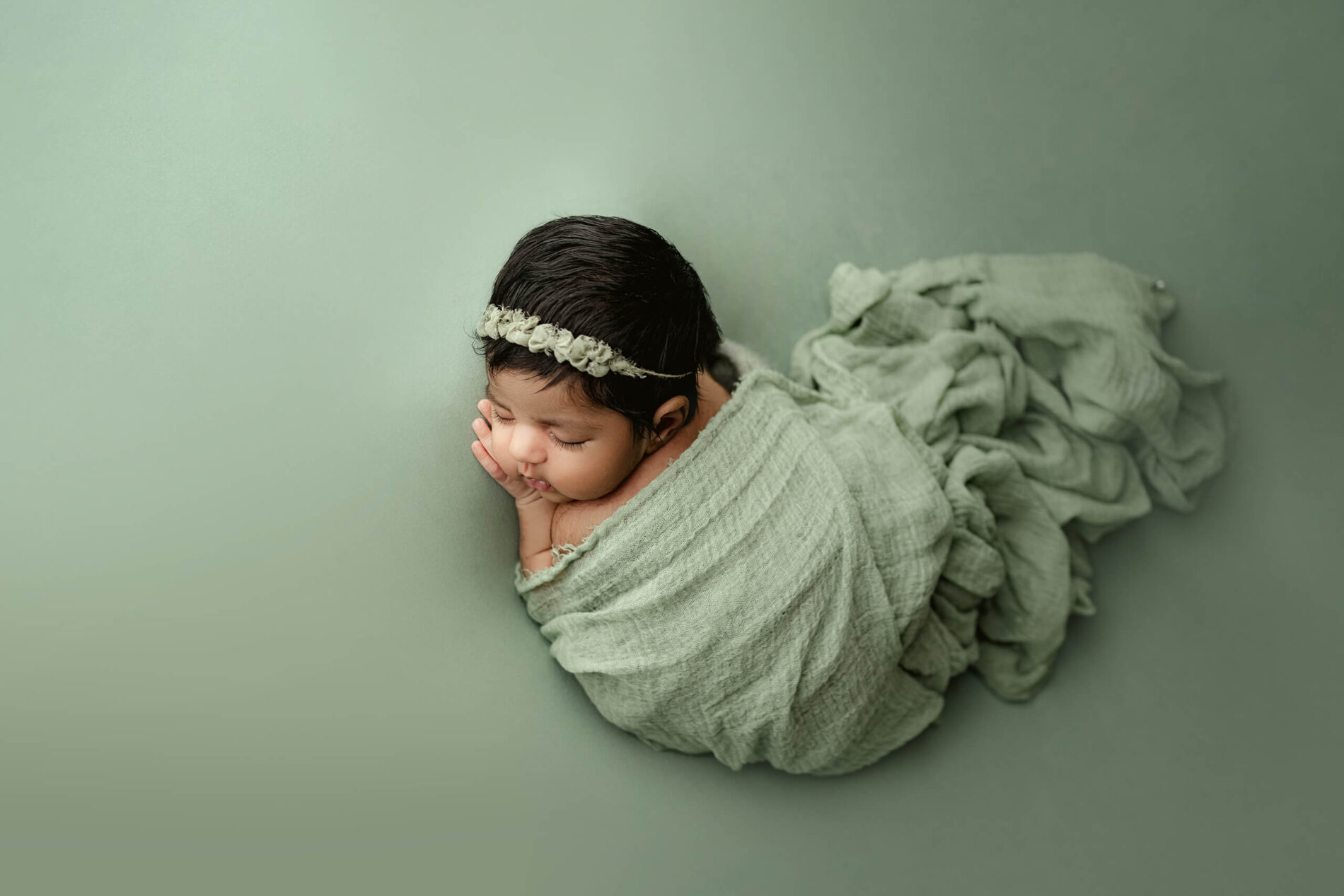 Newborn photo of a sleeping baby girl covered with green blanket and lying on green background