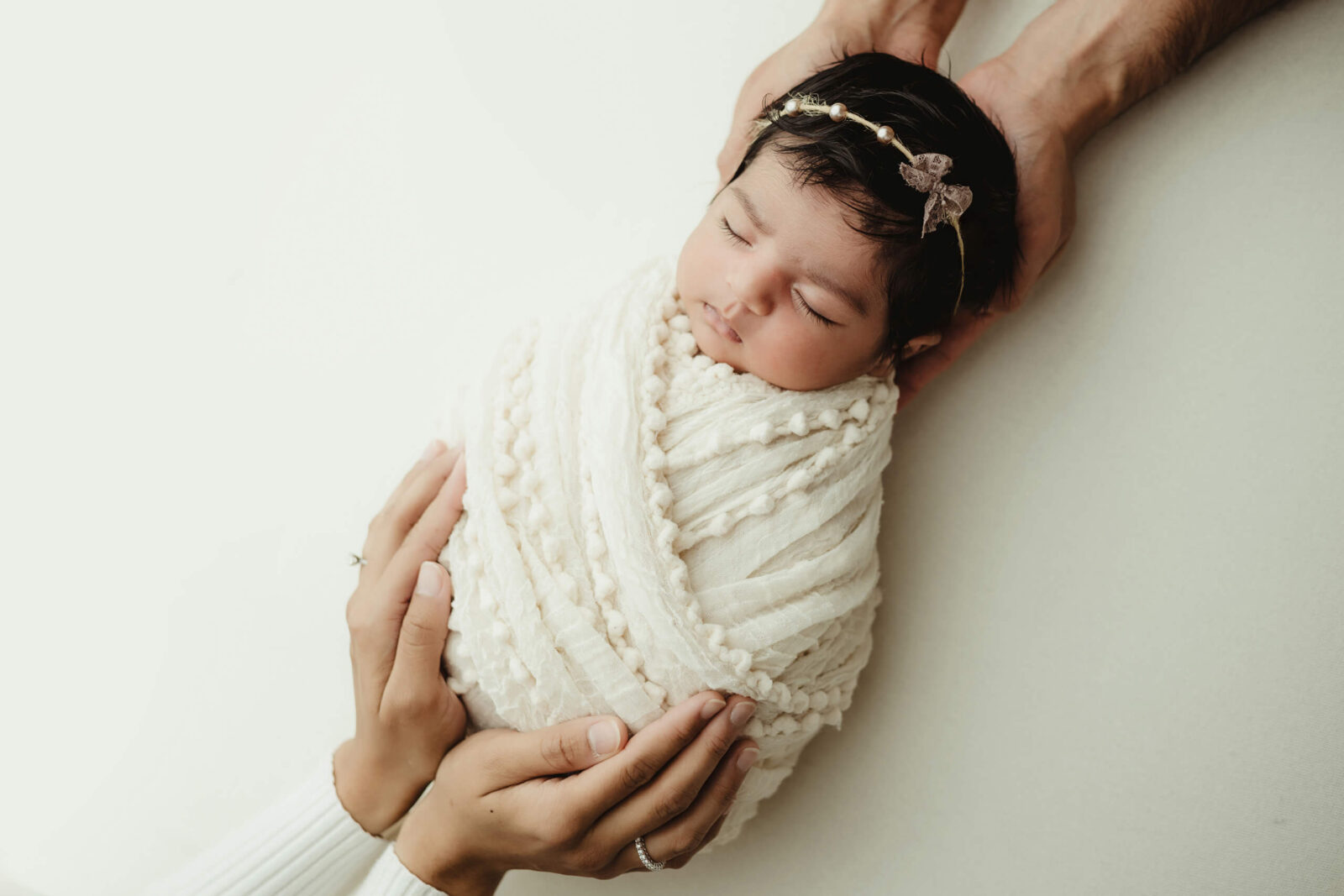 Unique newborn photography with parents, baby girl wrapped in white blanket with parents hands on her head and body