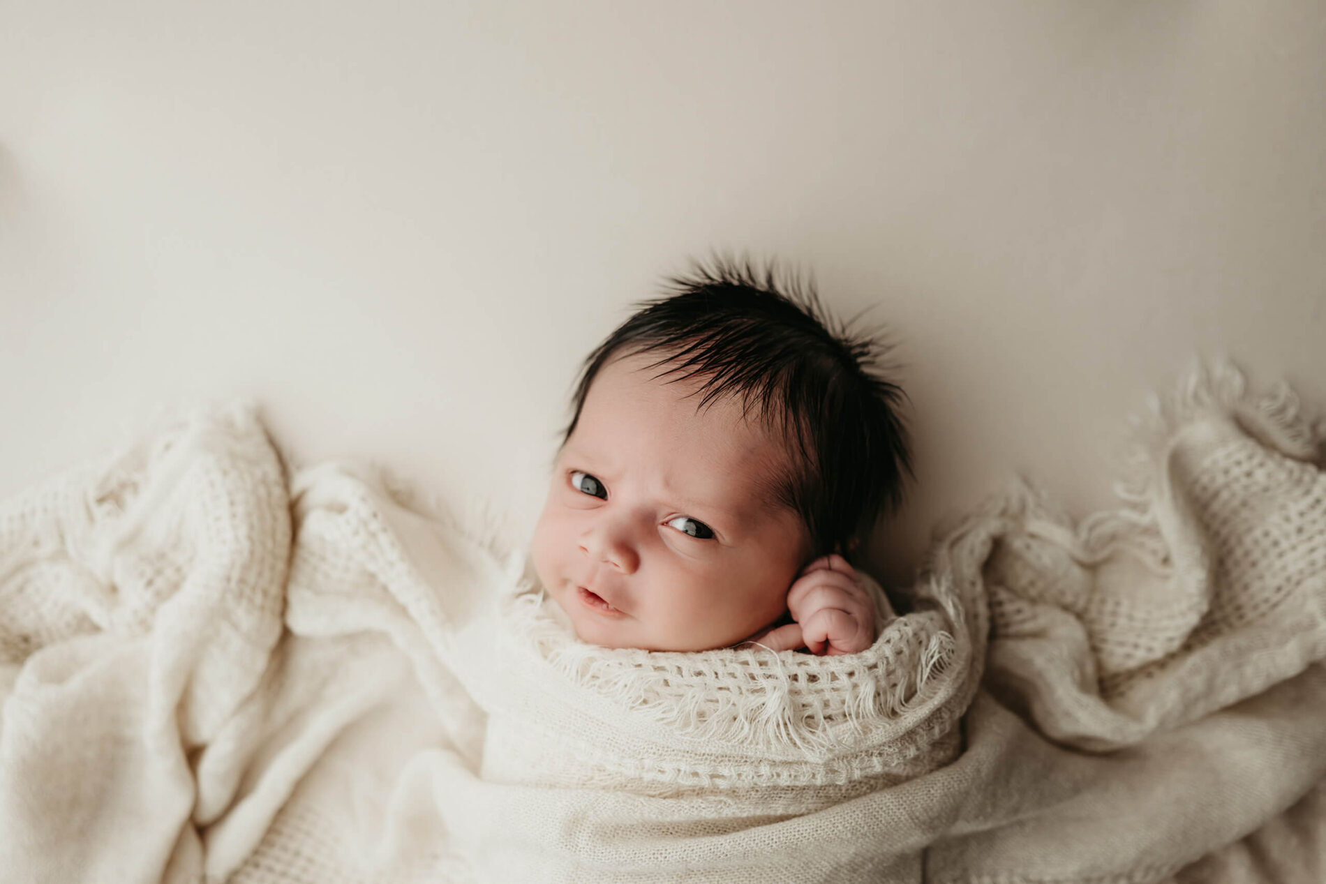 Alert baby boy covered with white blankets during newborn photo shoot