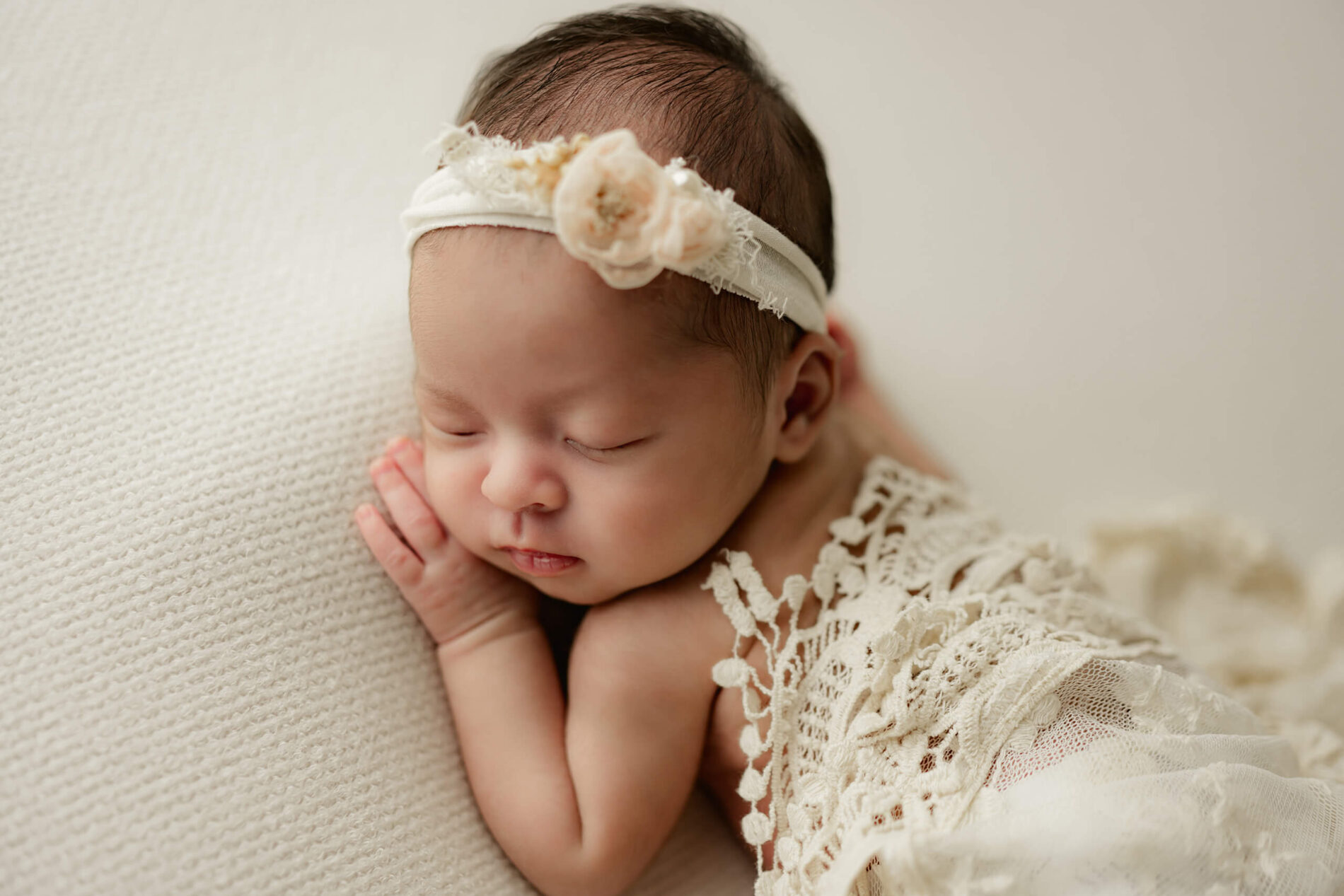 Sleeping baby girl wearing a beautiful headband during newborn photo shoot
