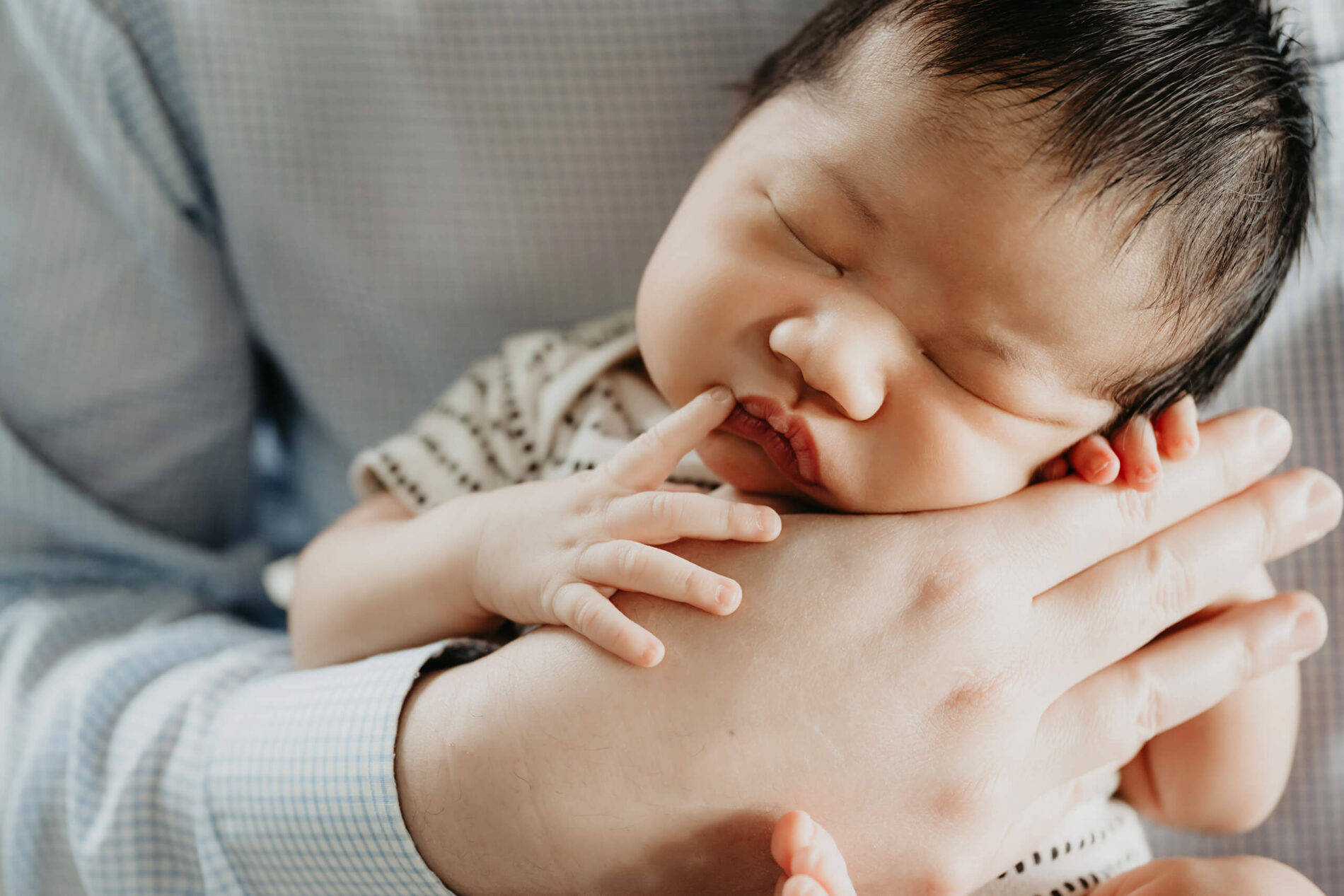 Newborn photo of newborn boy in dad's arms, close up on baby's face and dad's arms