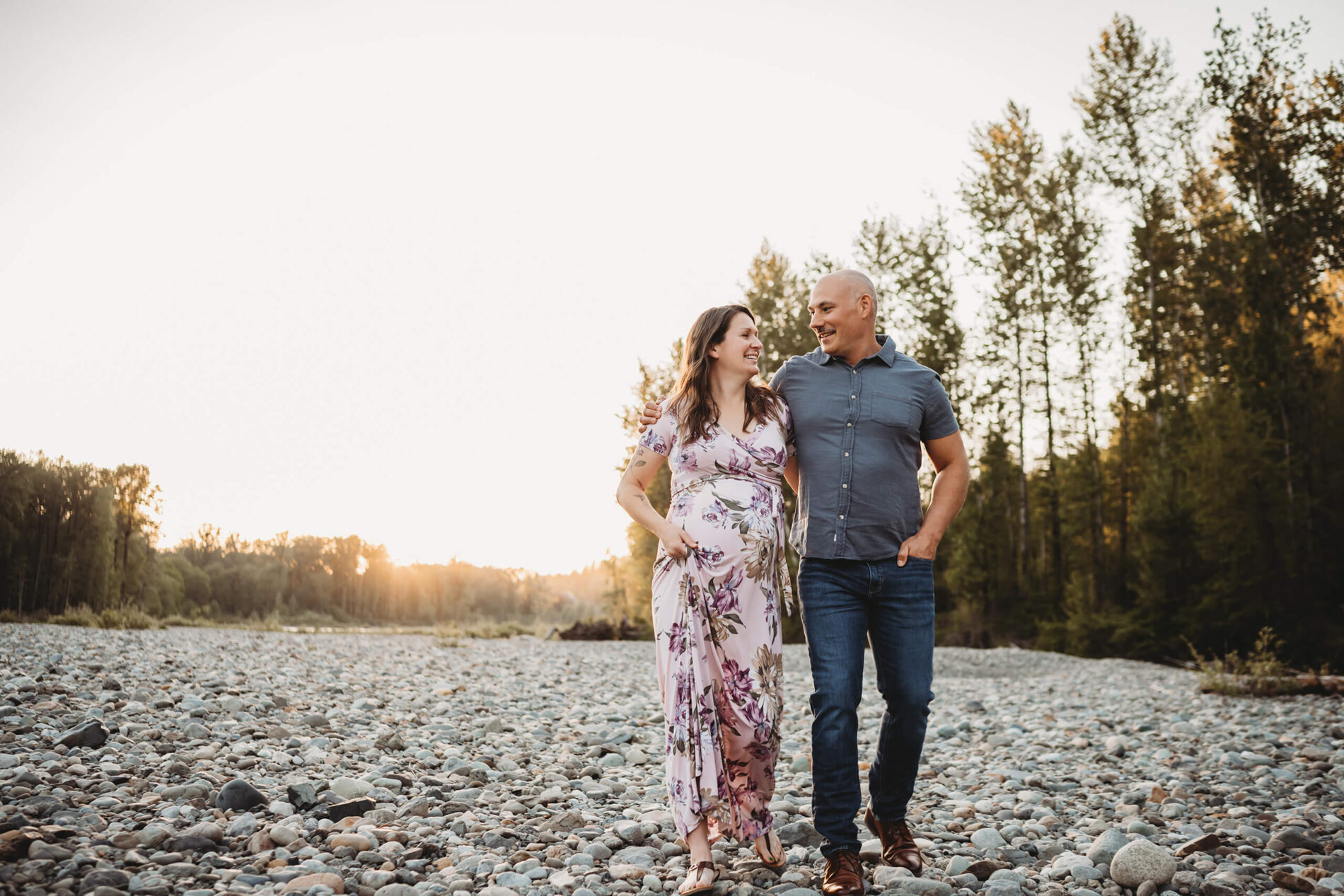 Posing idea for pregnancy photo shoot, young happy couple walking and talking on a riverbank
