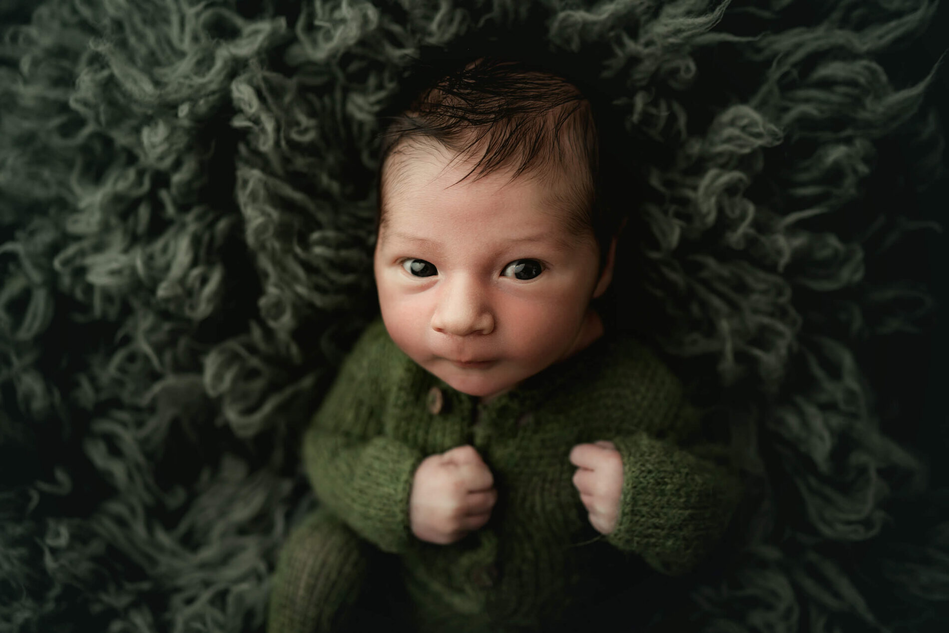 Studio newborn photography in Seattle, baby boy in green onesie lying on green rug, looking straight into the camera