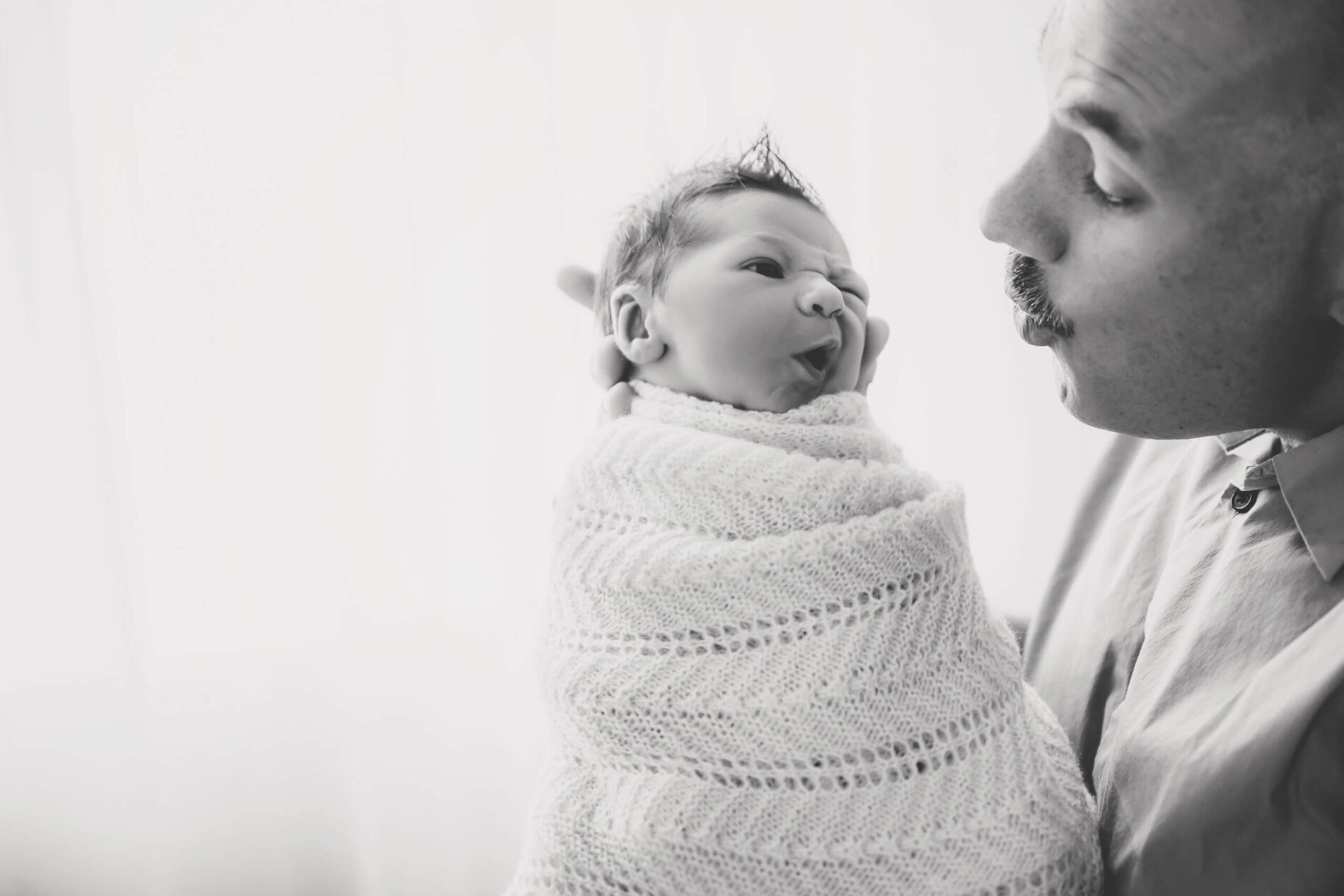Black and white photo of a dad playing with his newborn son