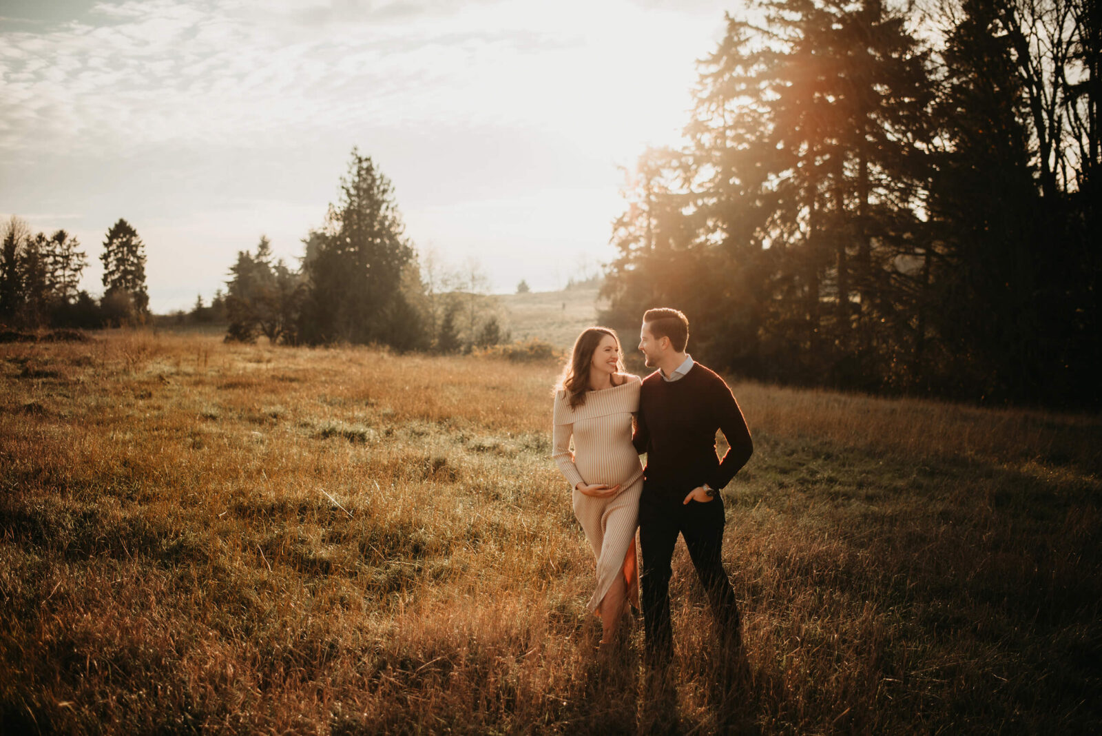 Seattle maternity photography, young couple hugging, walking through a filed at Seattle Discovery Park during sunset.