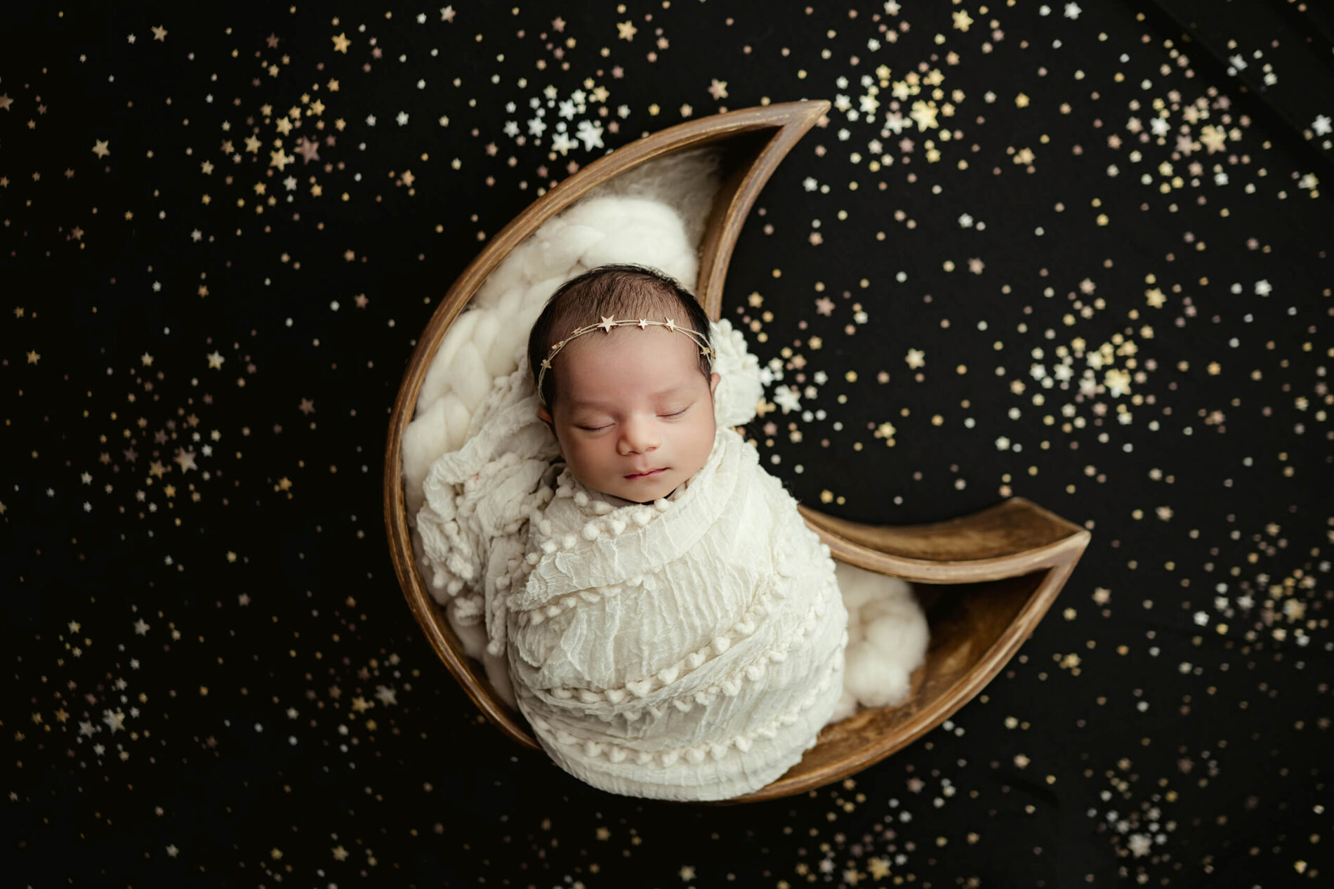 Newborn baby wrapped in a moon-shaped prop surrounded by stars during a studio newborn portrait