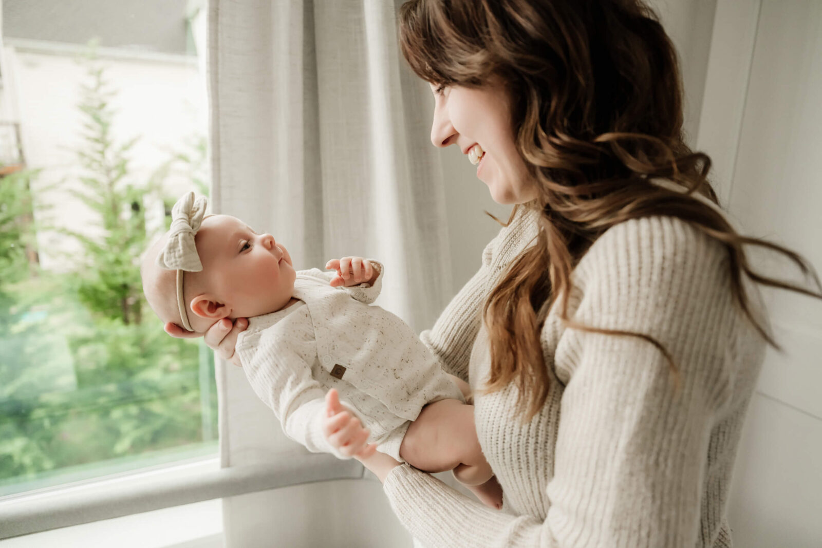 Mom holding her 3-month-old baby by the window during an in-home newborn photo session
