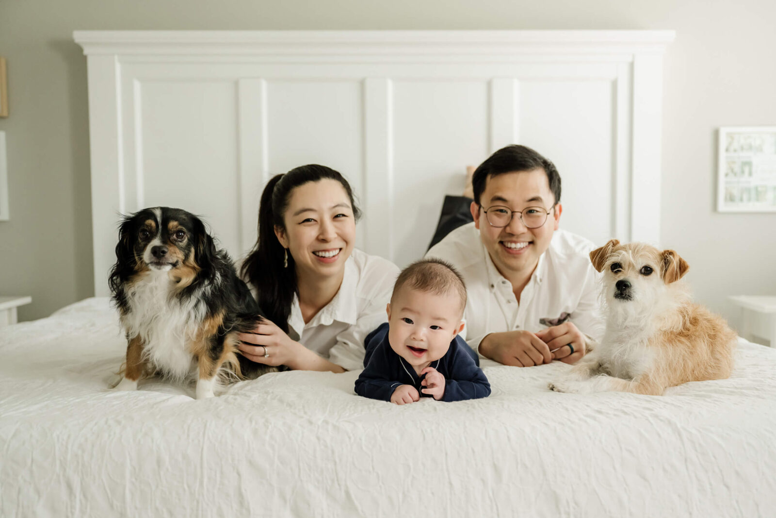 Family smiling with their 3-month-old baby and two dogs during an in-home newborn photo session