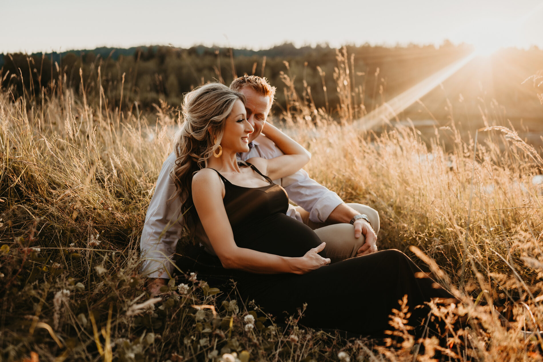 Couples maternity photo shoot in Bellevue, husband and wife sitting in a field of tall grass during summer sunset