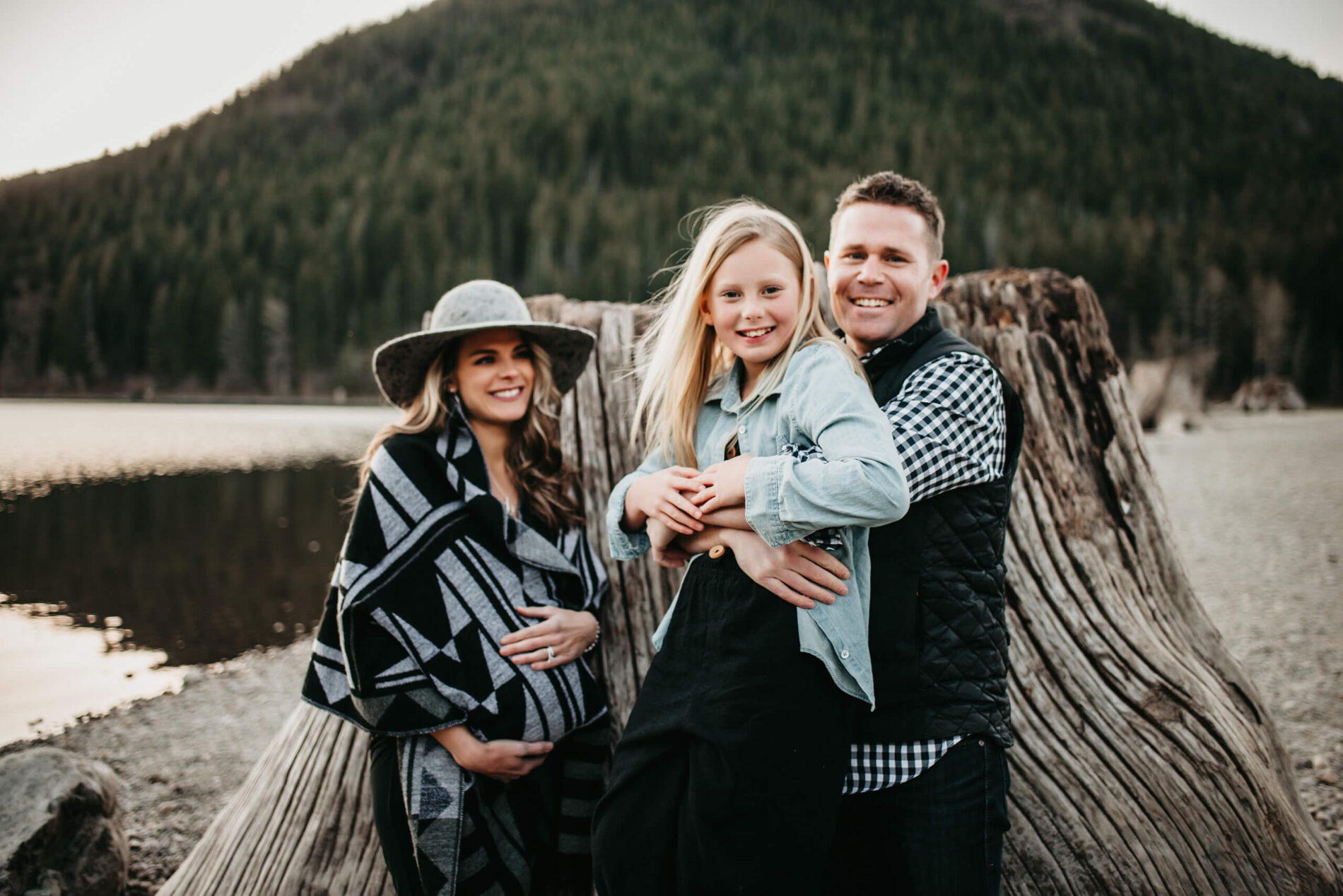 A happy family posing during maternity photo shoot, lake and mountains in the background