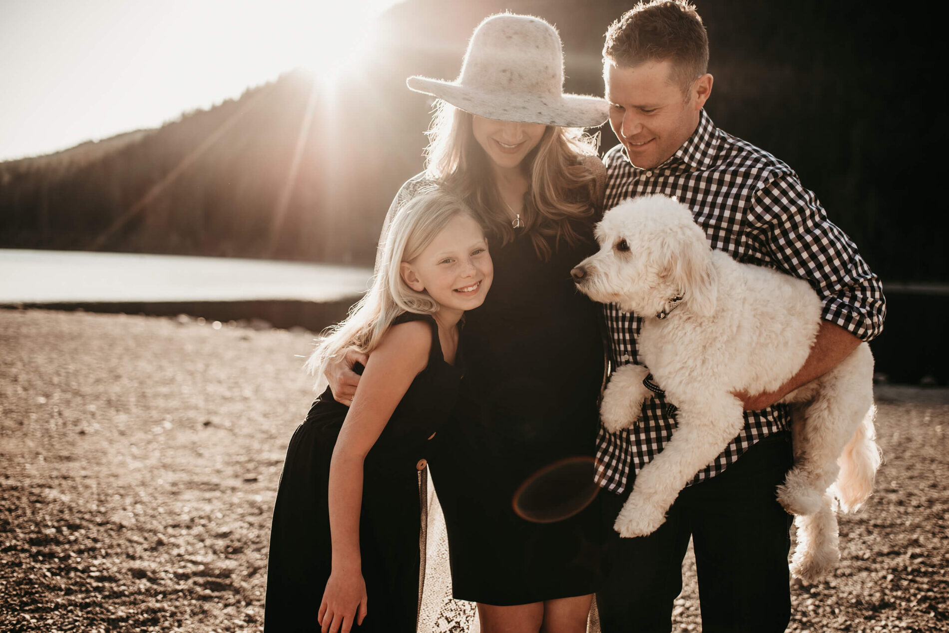 Family maternity photo shoot, dad and mom with their daughter and dog on a beach of a lake