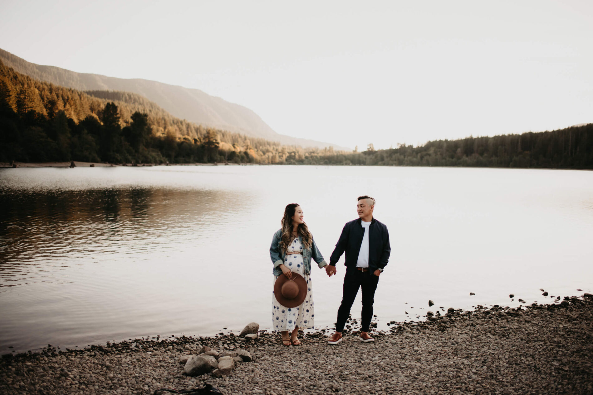 A young couple holding hands during a maternity photo shoot in Seattle, lake and mountains in the background