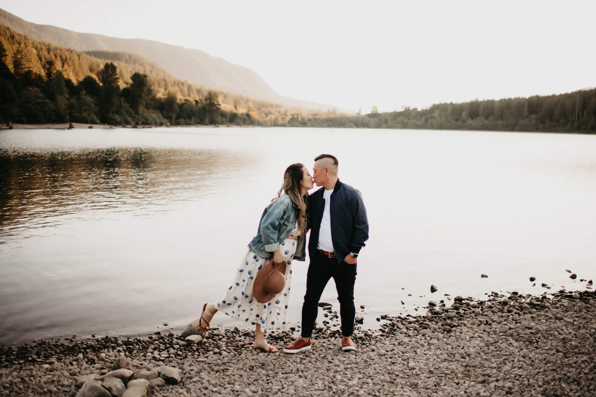 A young couple kissing during a maternity photo shoot in Seattle, lake and mountains in the background