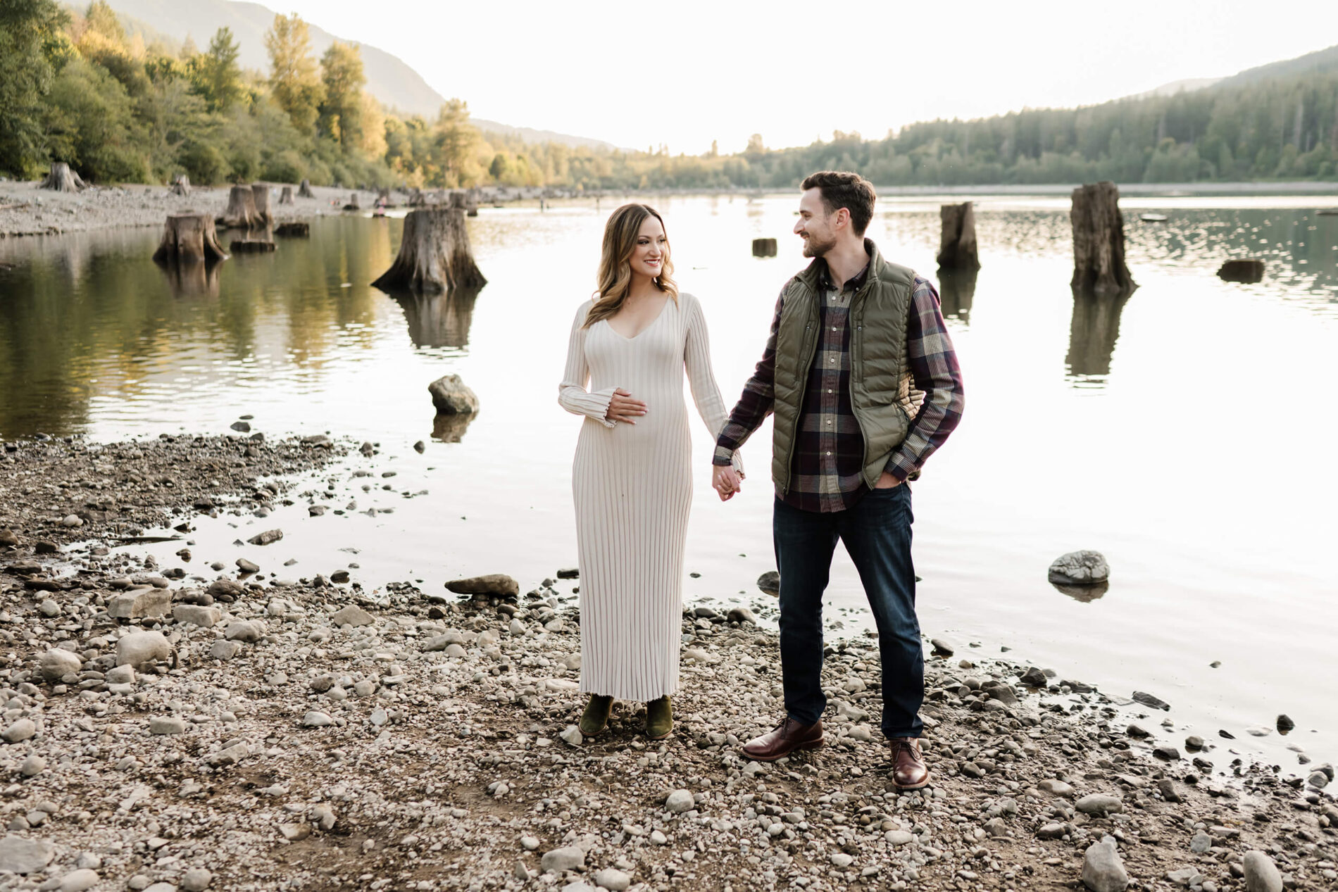 A couple naturally posed by a lake with mountain views in the background