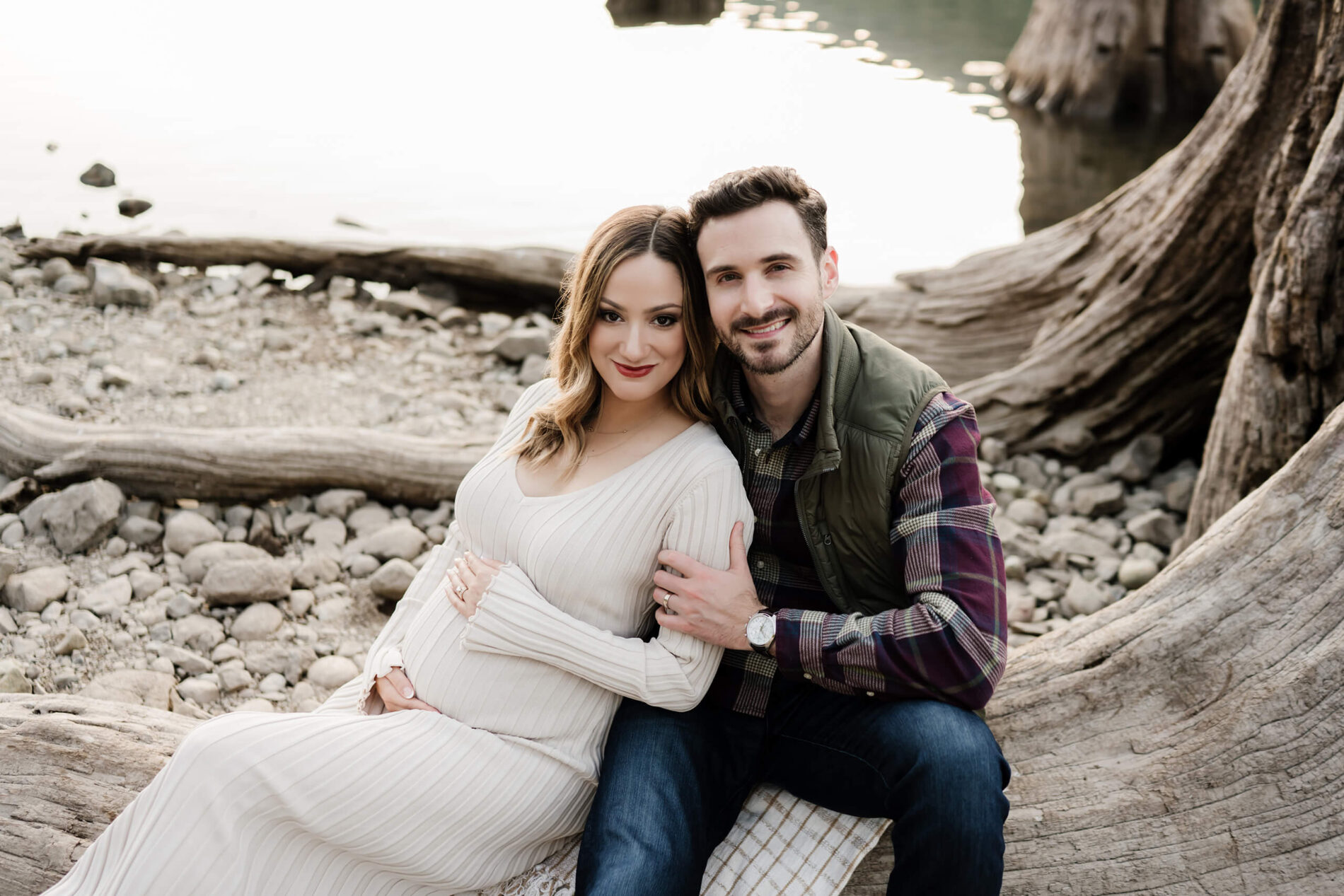 A smiling couple sitting on a large tree stump during maternity photo shoot in Seattle