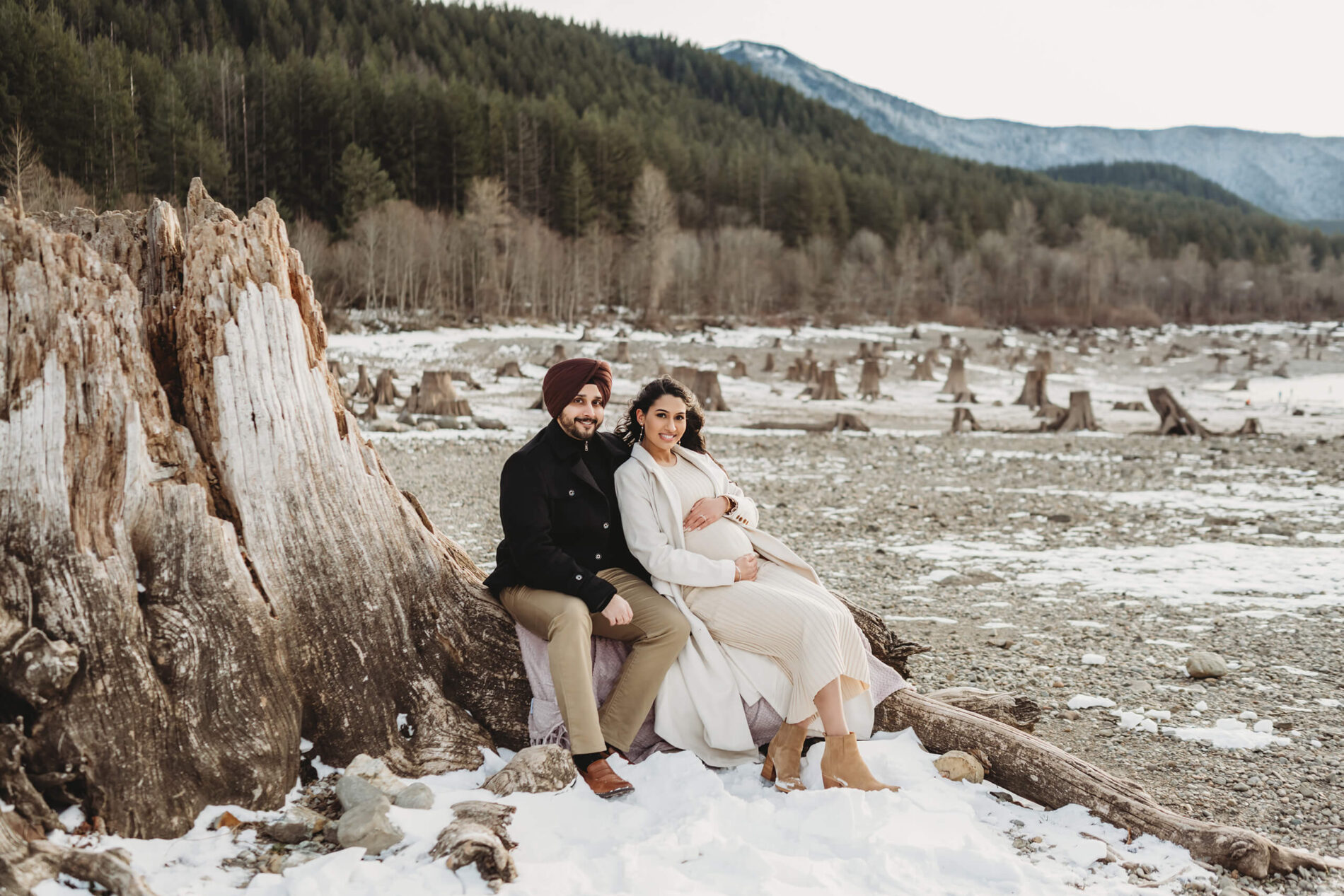 A young couple posed on a large tree trunk during a maternity photo shoot in Seattle