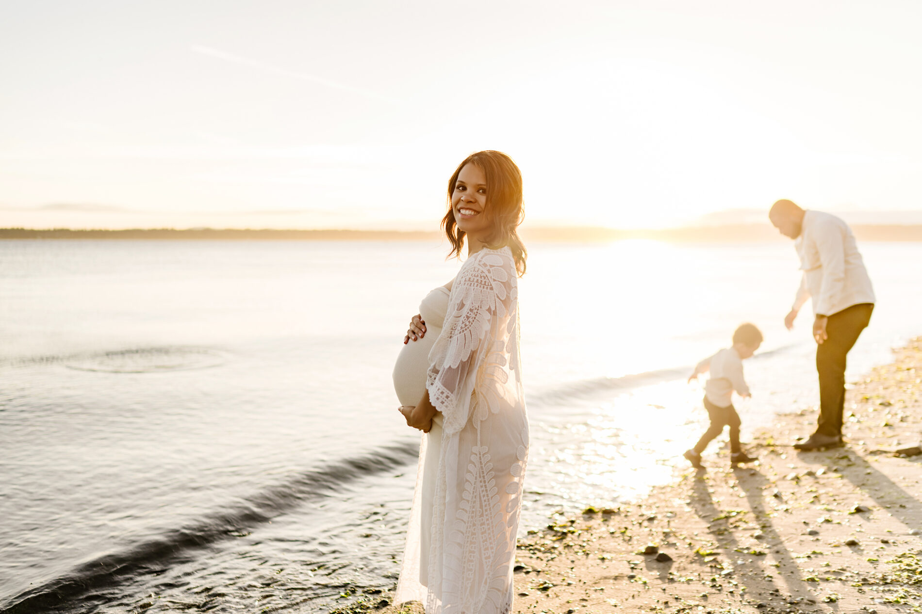 Seattle beach family photo shoot, mom in the foreground with dad and son playing in the background