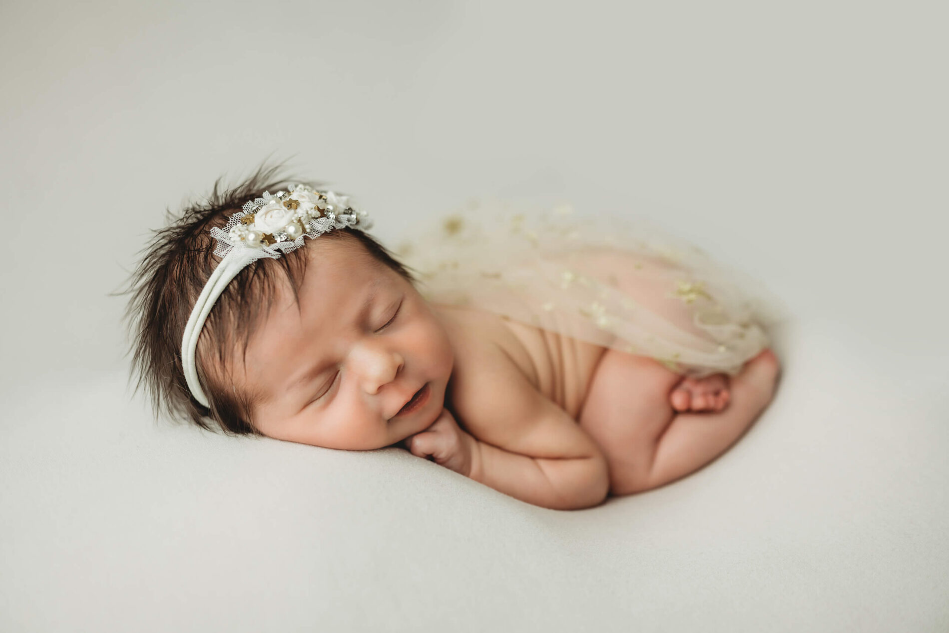 Natural newborn photography in Kirkland. Sleeping baby girl wearing a headband, smiling in her sleep.