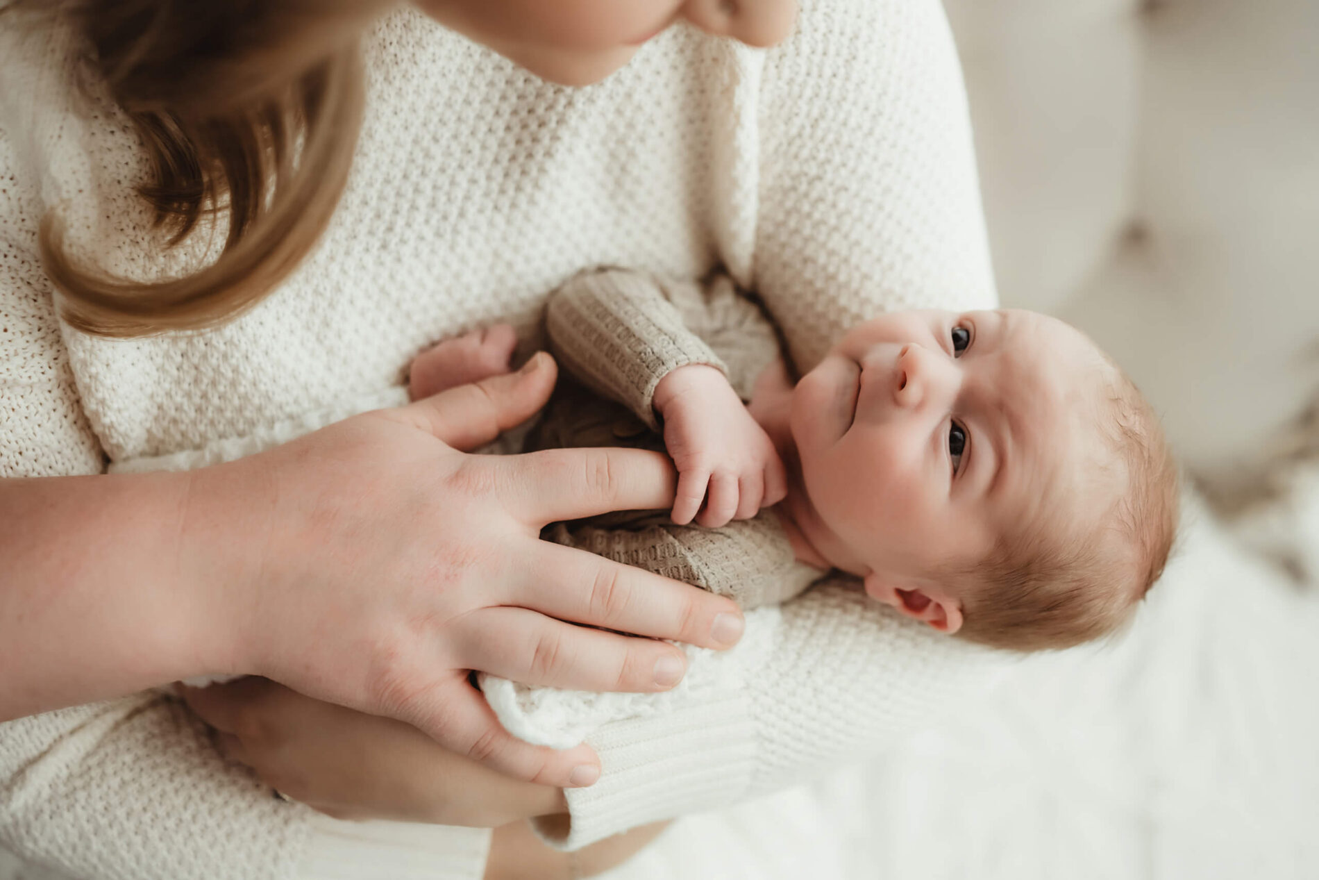Natural newborn photography, baby boy looking up at mom, grabbing her finger