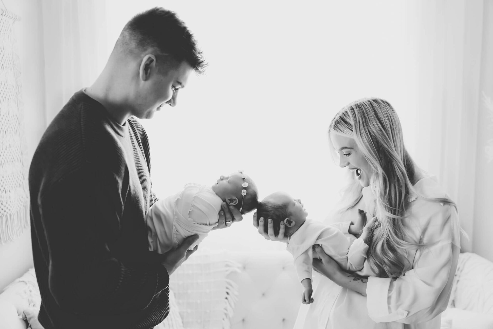 Classic black and white family newborn photo with twins. Mom and dad holding their babies, backlit with bright light from a window