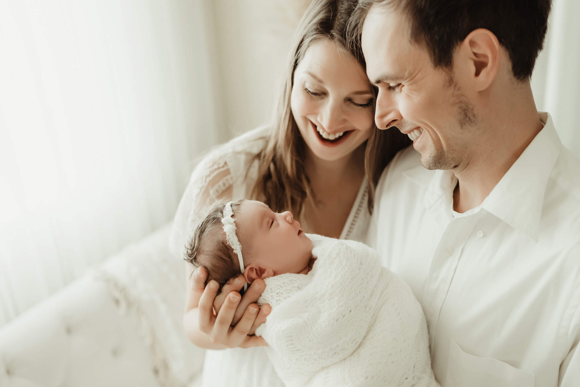 Unique newborn photography with parents in Bellevue. Smiling mom and dad, looking at their smiling infant.