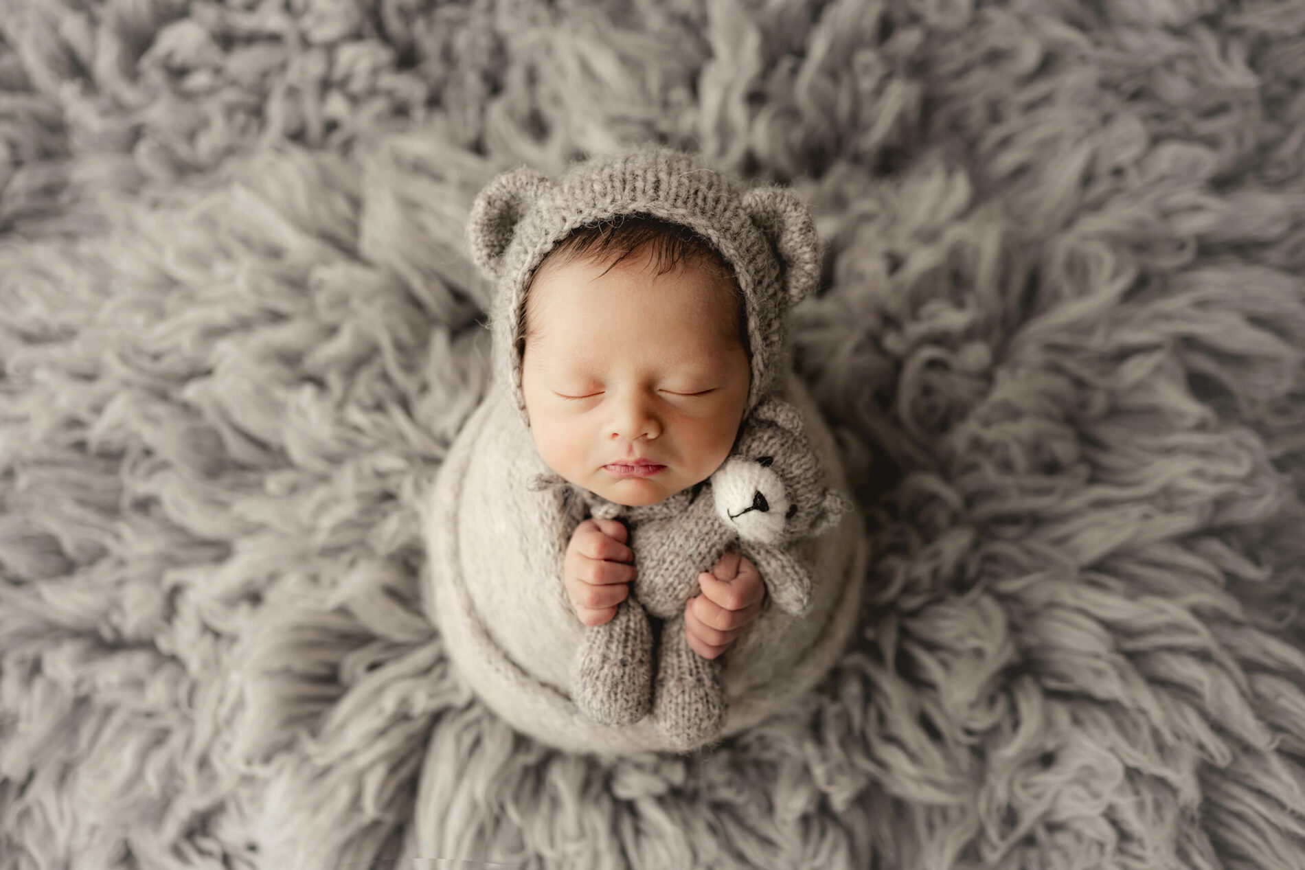 Newborn photography with props. Baby boy masterfully wrapped, posed sleeping holding a stuffed bear.
