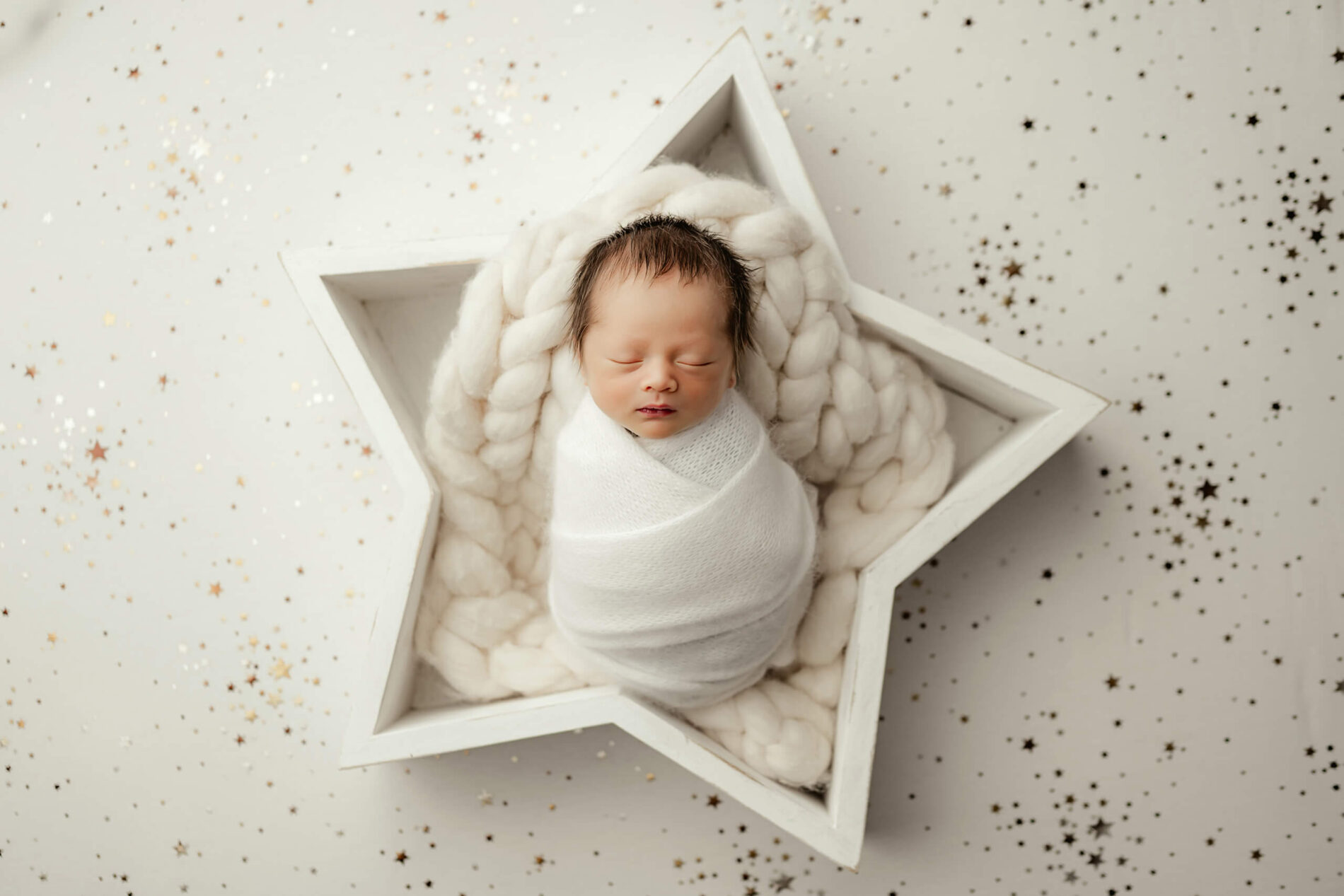 Unique newborn photography. Infant boy posed masterfully in a star-shaped prop during a photo shoot.