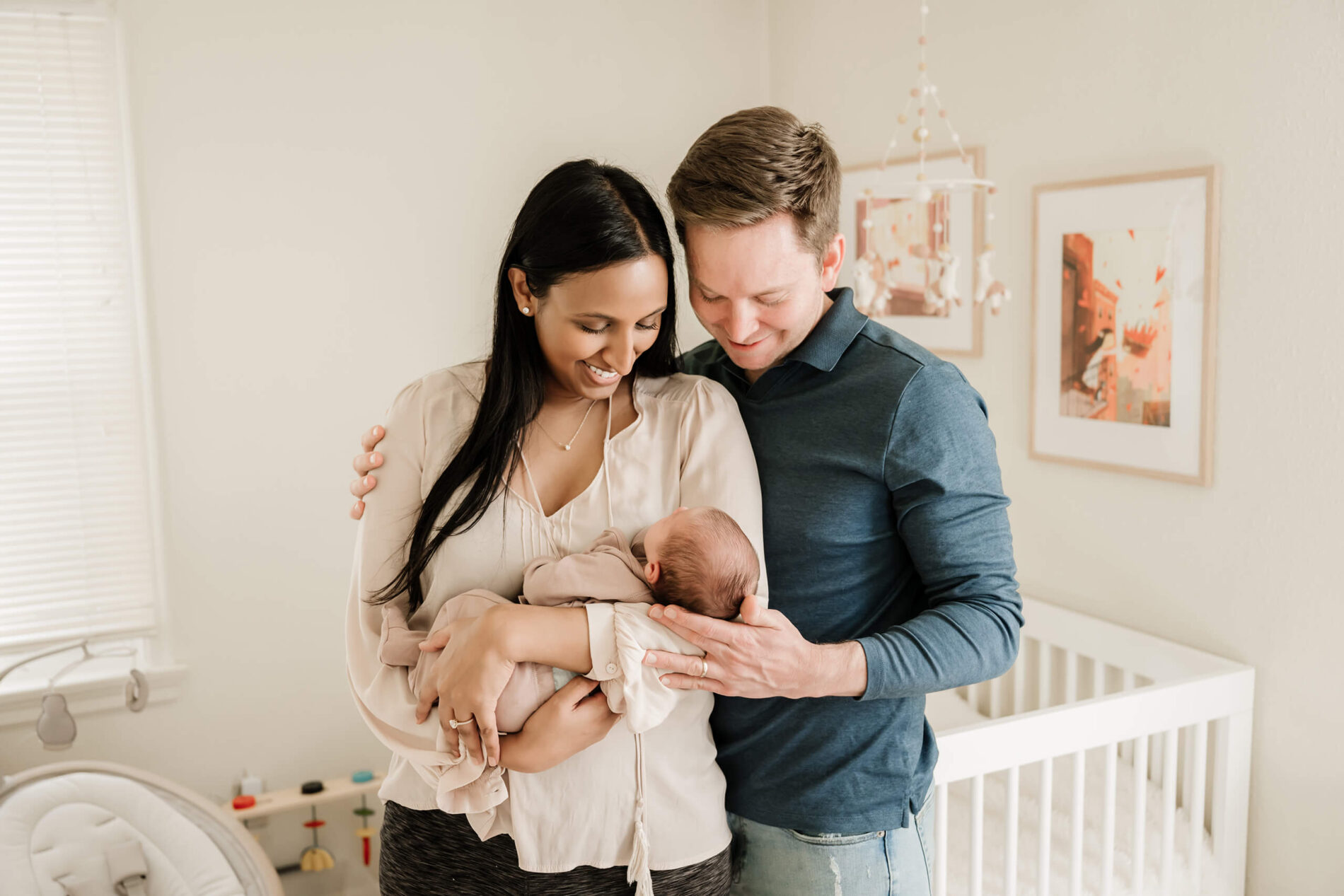 A couple holding their baby in the nursery, smiling. Kirkland in-home newborn photography.