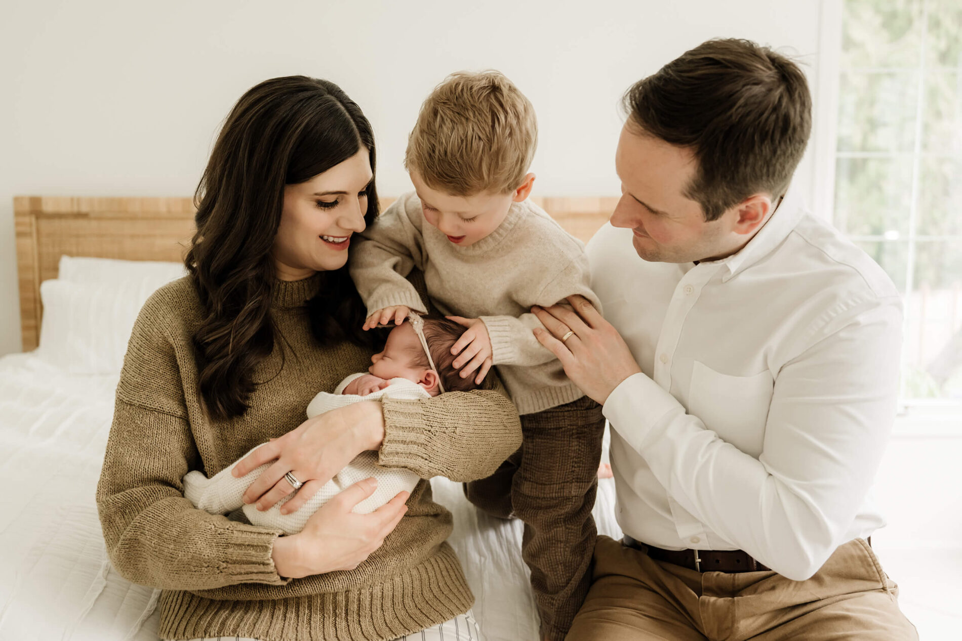 Family newborn photo in a bedroom. Parents with toddler and newborn daughter sitting on a bed.