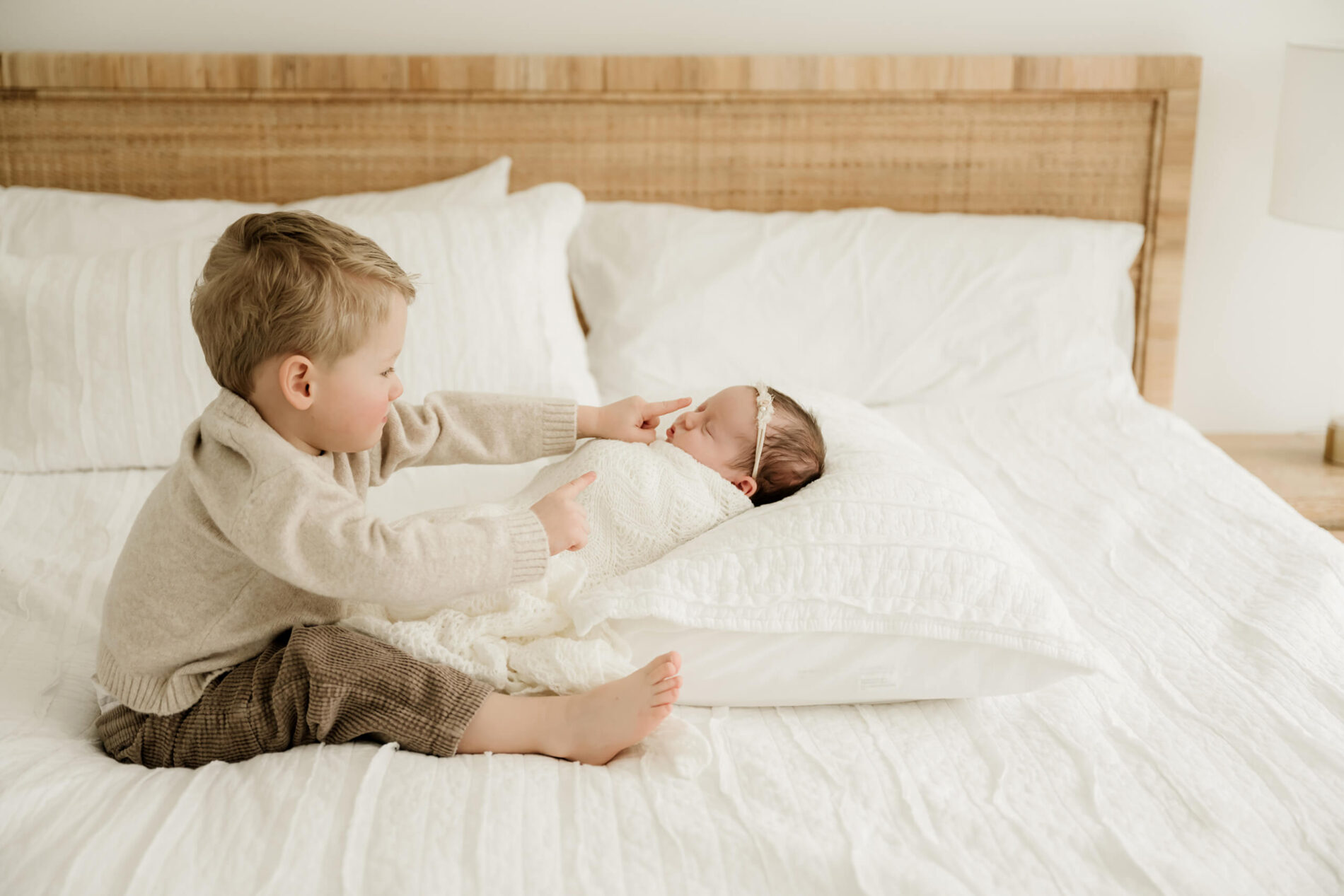 A sample pose from a Kirkland area lifestyle newborn photo session. A toddler sitting on a bed, touching the nose of baby sister. Charming family moment captured.