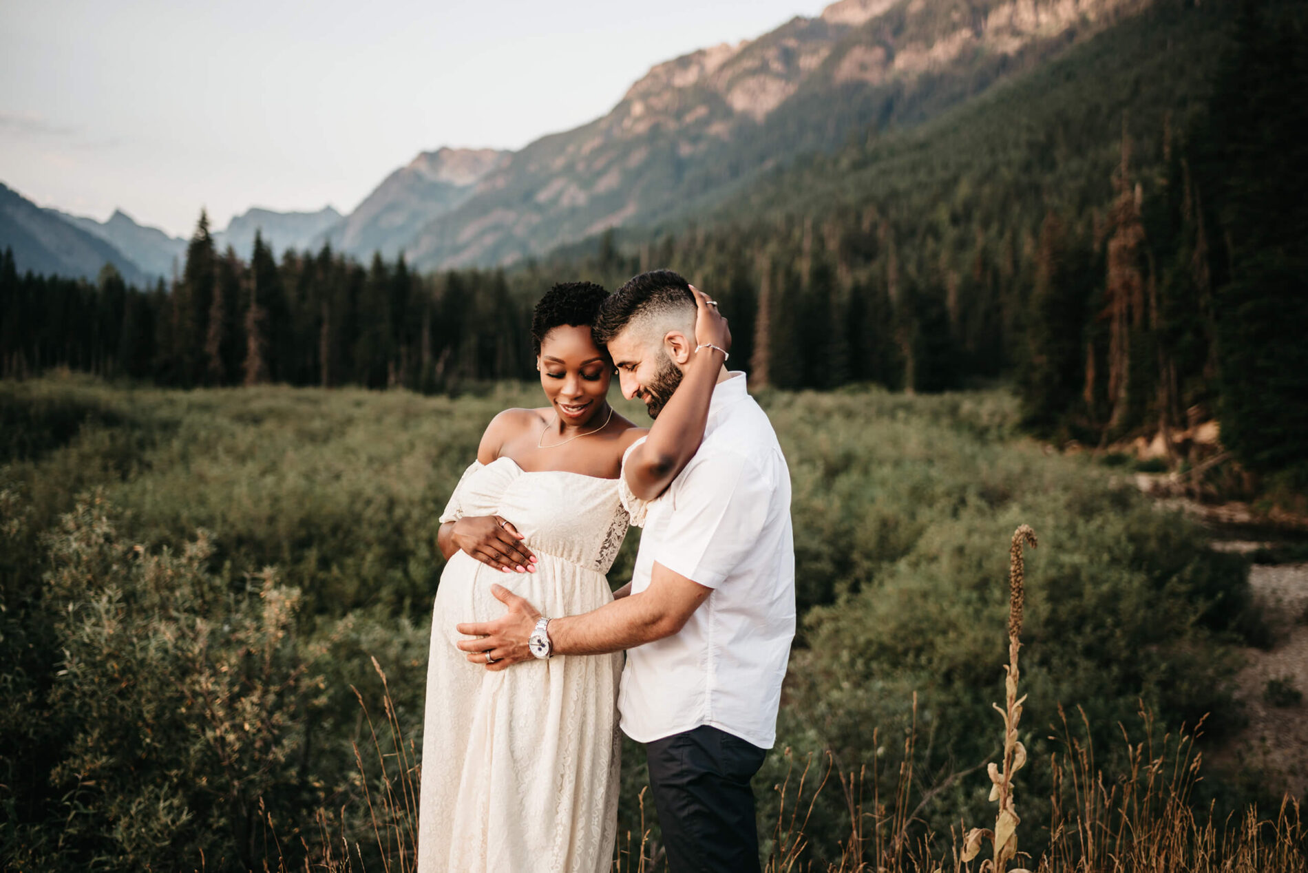 An example of a couples pregnancy photoshoot in Seattle, young happy couple in a field with Cascades in the background