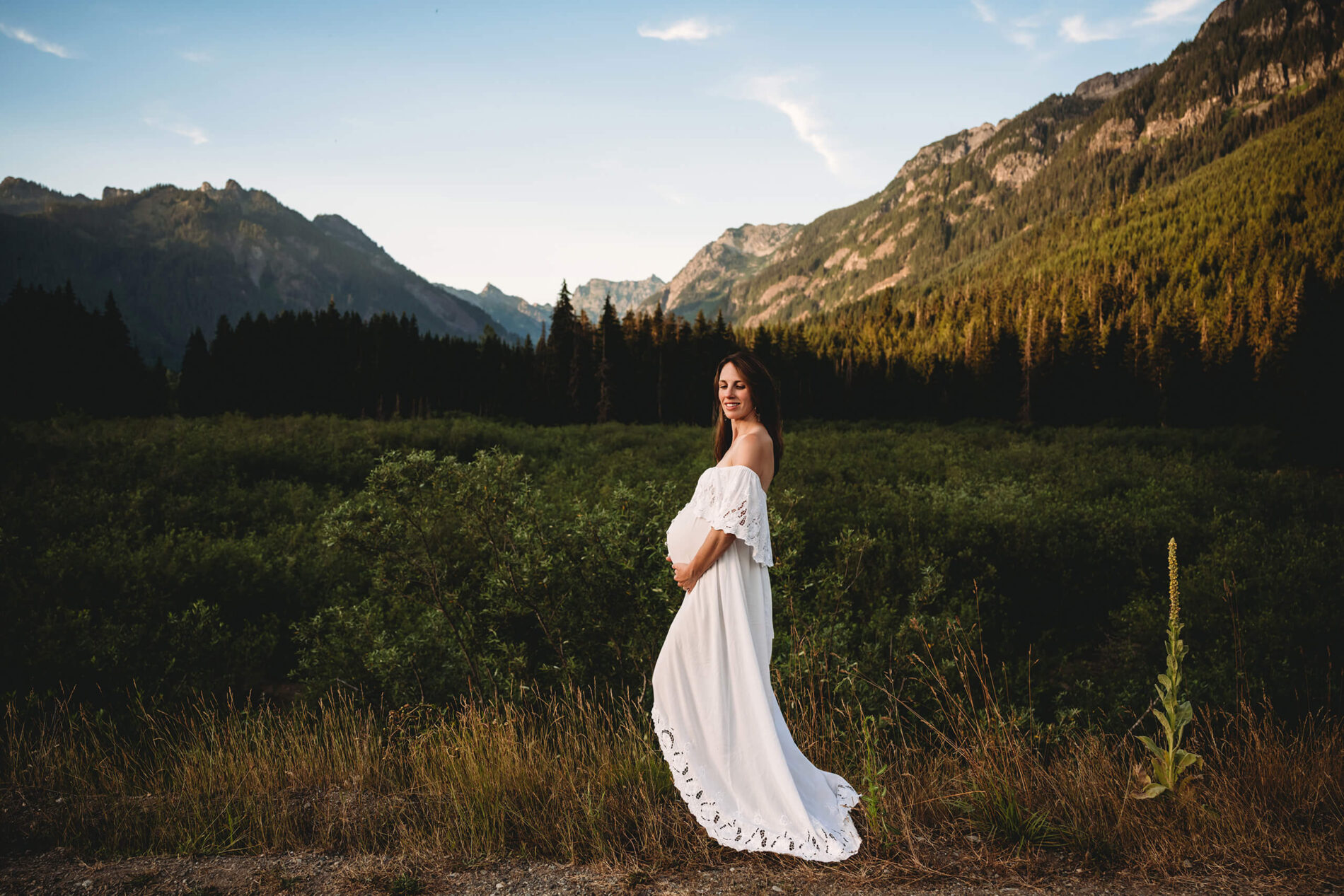 Natural posing idea for maternity photo in Seattle, pregnant woman in off-the-shoulder white dress, mountains in the background