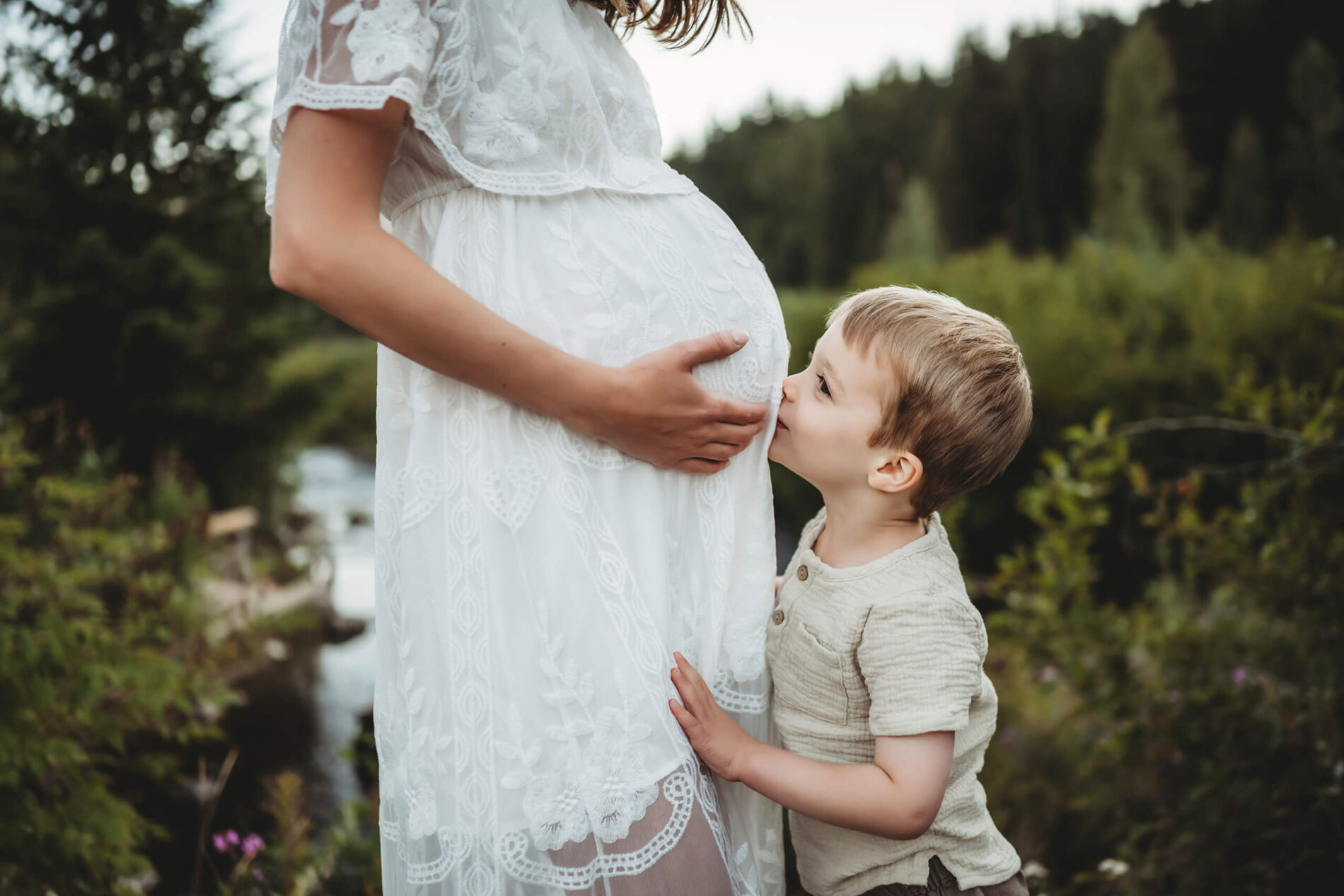 Posing idea for a maternity photoshoot, pregnant woman in a dress, sibling kissing mom's belly
