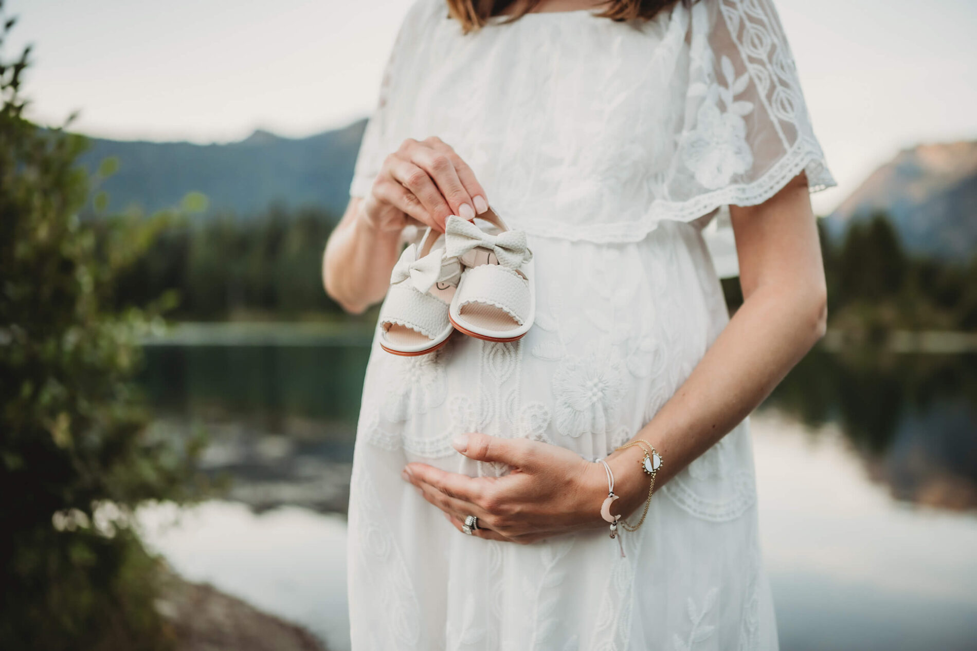 Posing idea for a maternity photoshoot, pregnant woman in a dress holding tiny shoes