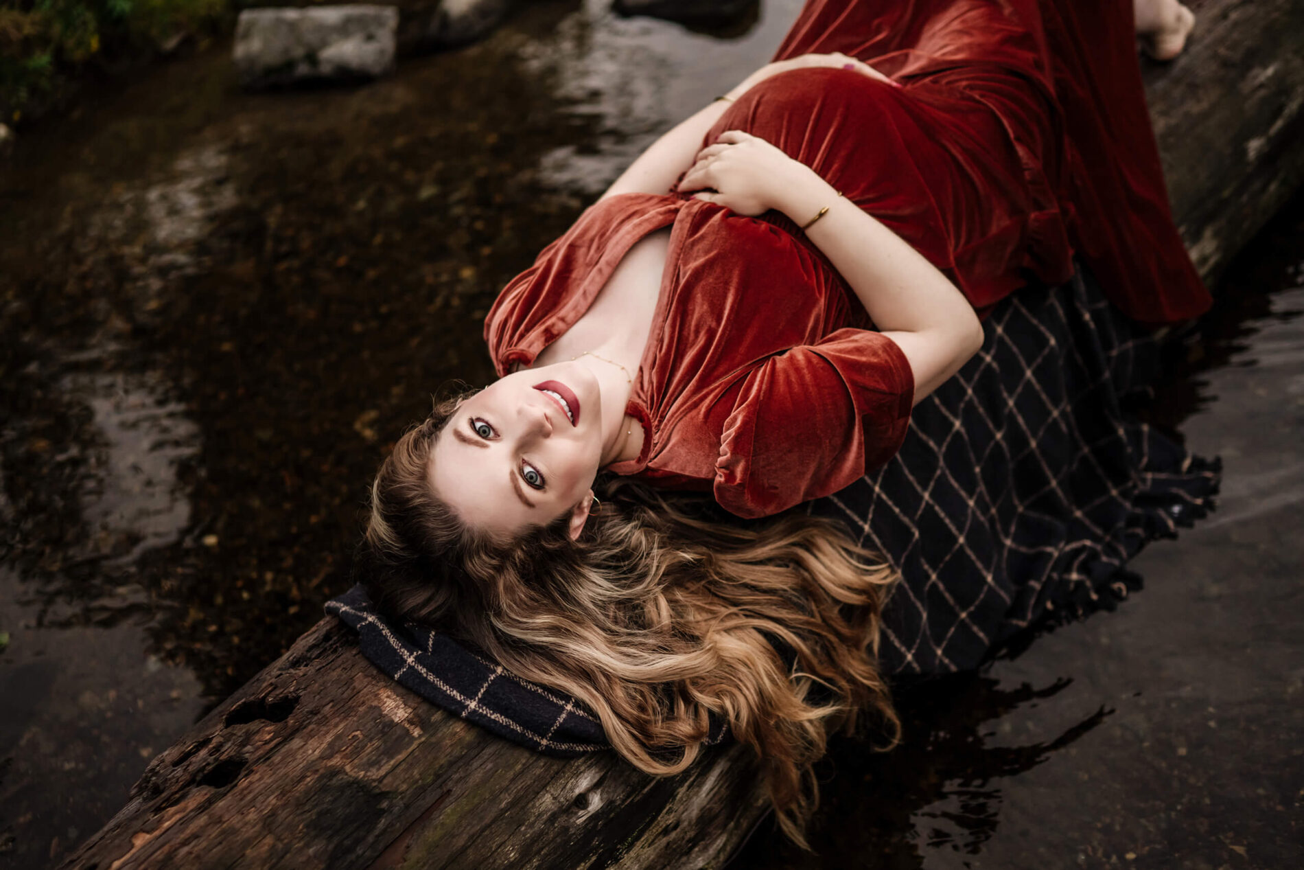 Unique posing idea for maternity photo in Seattle, pregnant woman lying on a fallen tree in a river