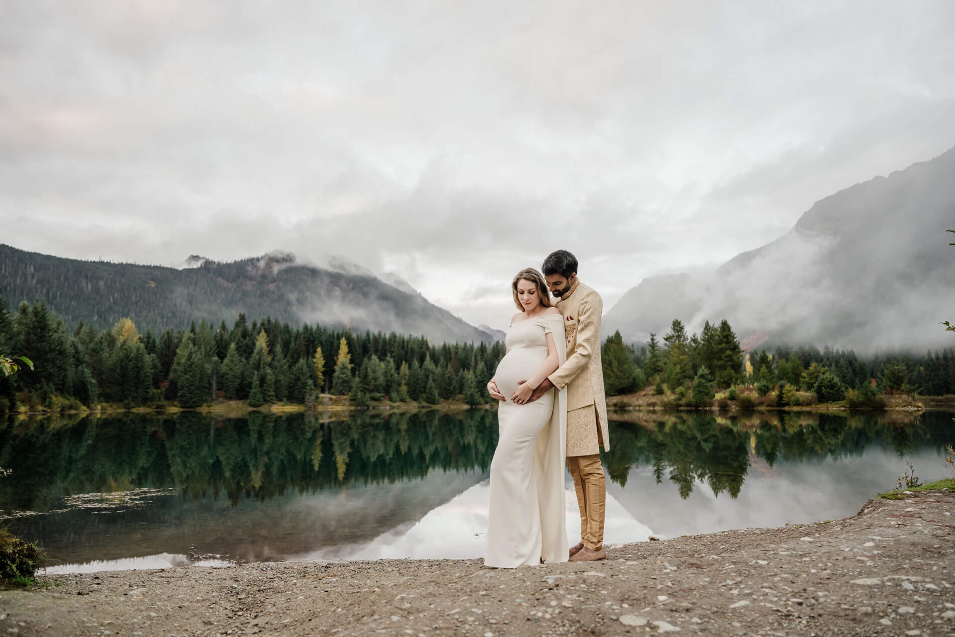 A couple wearing cultural clothing during a Seattle maternity photoshoot in front of a pond with mountains in the background
