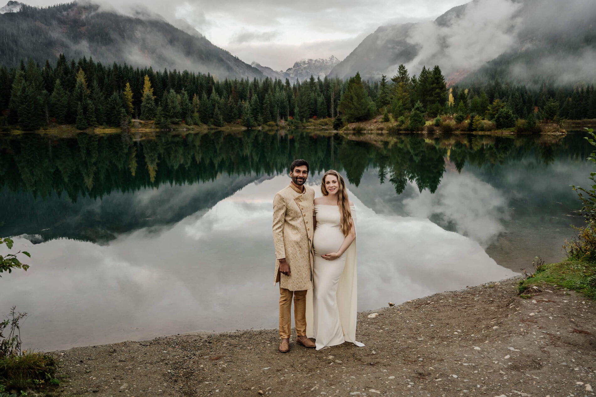 A couple wearing cultural clothing during a Seattle maternity photoshoot in front of a pond with mountains in the background