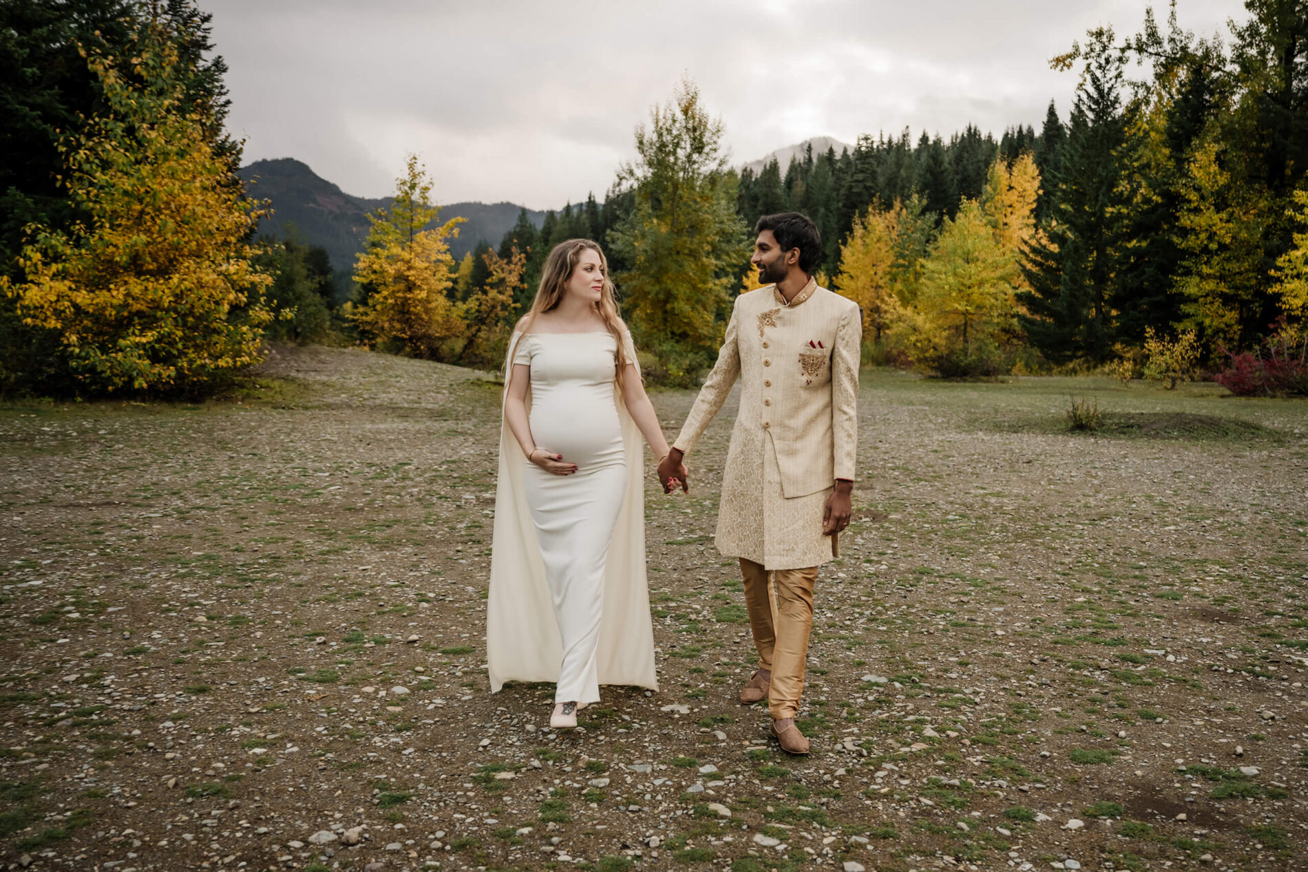 A couple wearing cultural clothing holding hands during a Seattle maternity photoshoot with mountains in the background