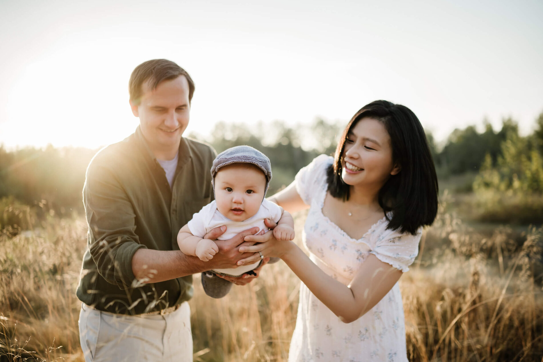 Family of 3 photo idea. Mom and dad holding their son in a field during a beautiful sunset.