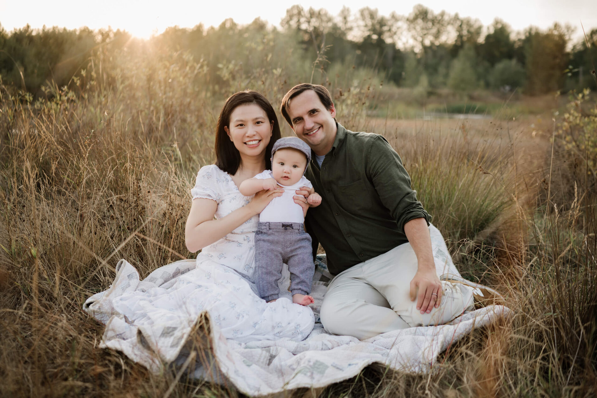 Family portrait of mom, dad and son sitting on a blanket in a field of tall grass.