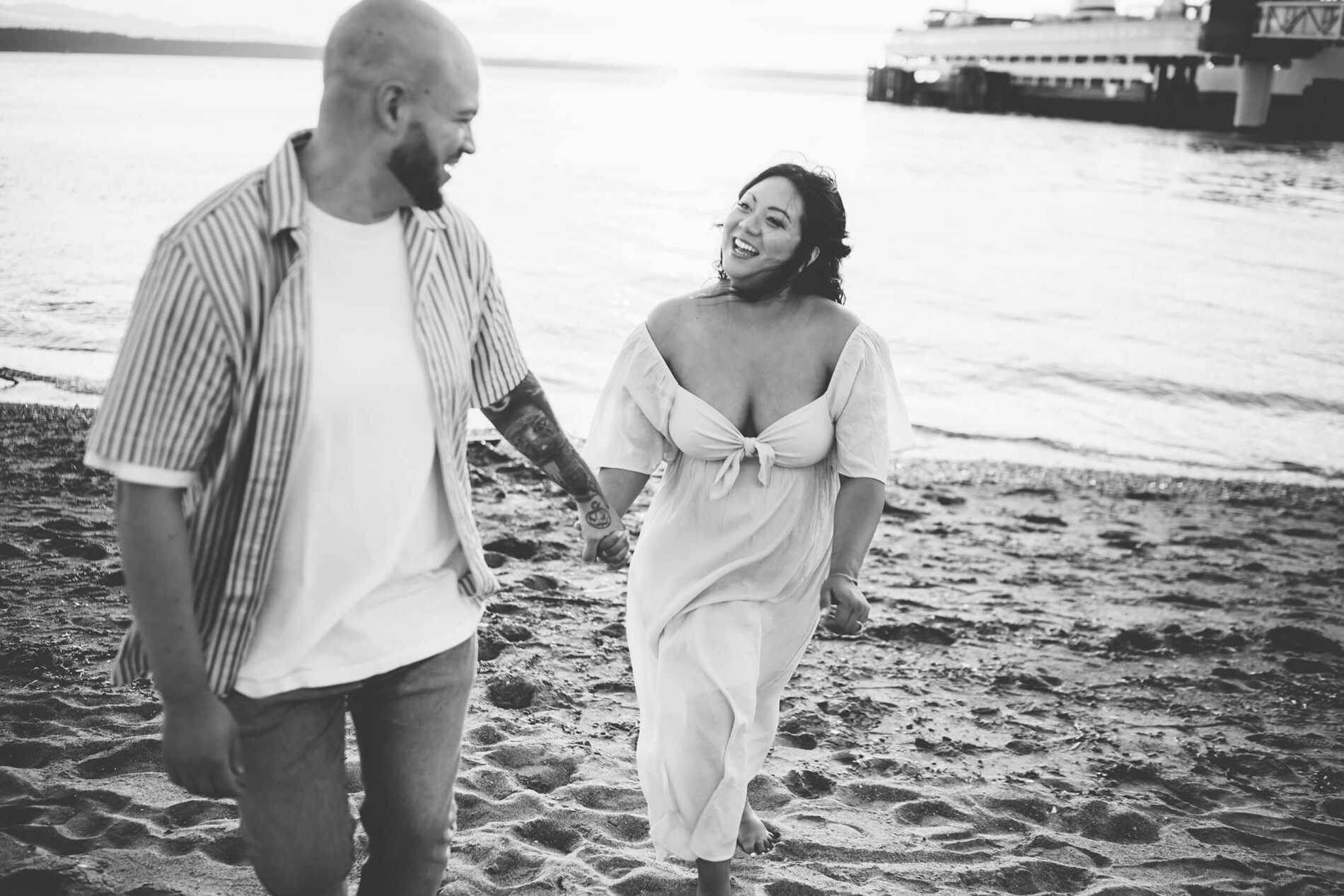 Black and white maternity photo of a couple walking on a beach, looking at each other, in Edmonds, WA