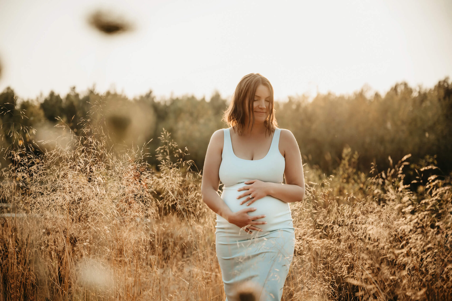 Happy woman in a field with tall grass during maternity photoshoot