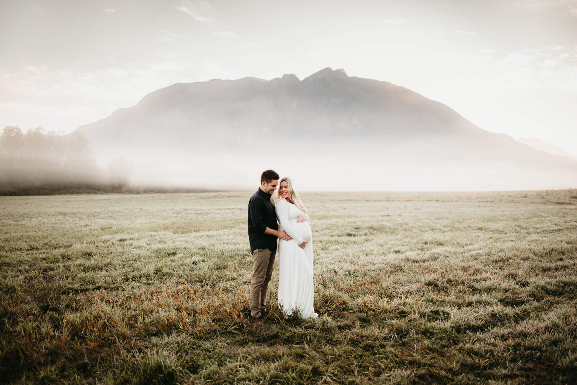 A couple in an open field during sunrise maternity photo session in Seattle area with Mt. Si in the background